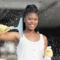Woman cleaning a window with a squeegee and spray bottle, smiling, wearing yellow gloves.