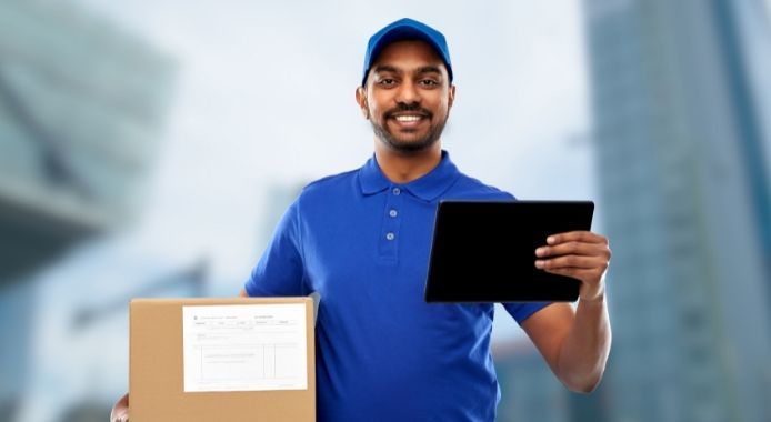 Delivery person holding a package and tablet in a city street, smiling.