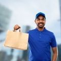 Delivery person holding a brown paper bag, smiling; in front of a city background.