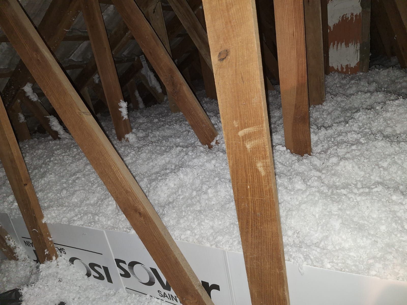 Intérieur du grenier avec poutres en bois et isolation blanche, probablement en cellulose.