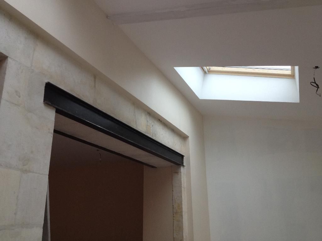 Vue intérieure montrant une ouverture rectangulaire surmontée d'une poutre sombre.