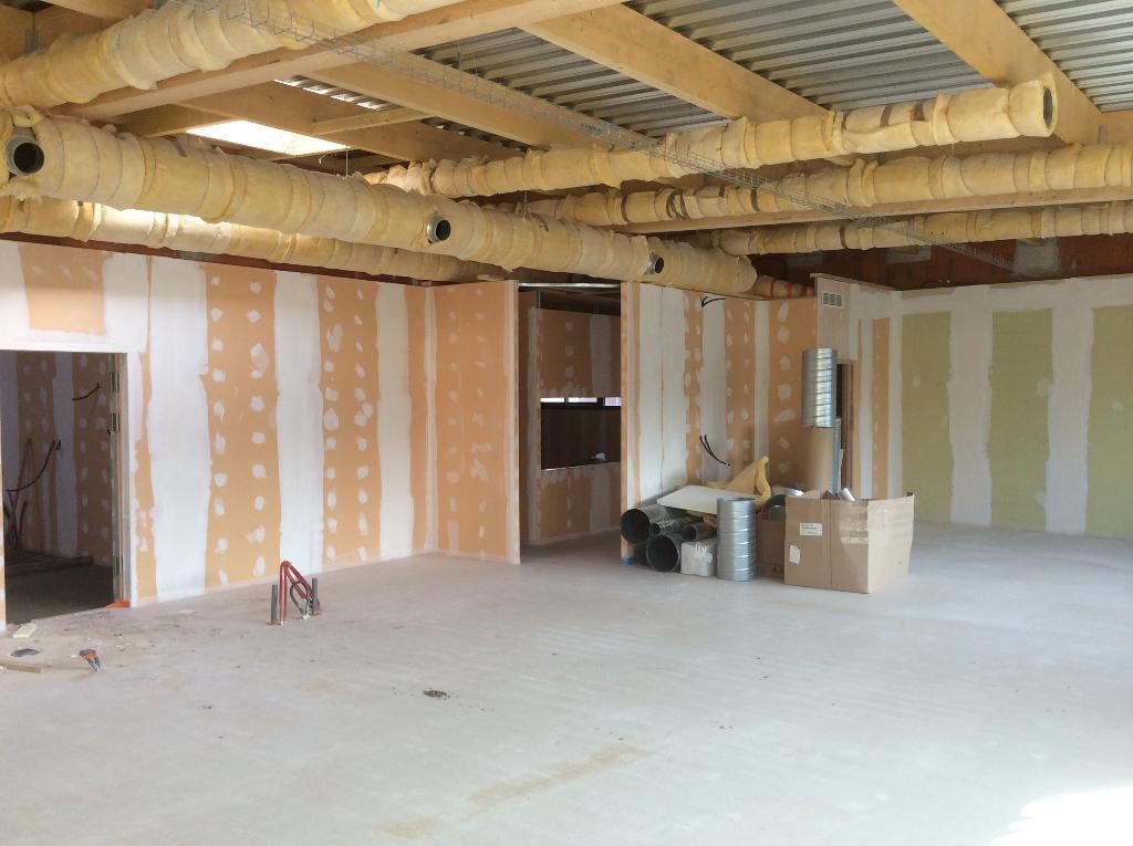 Intérieur d'une pièce en construction, avec poutres et conduits apparents, cloisons sèches partiellement installées.