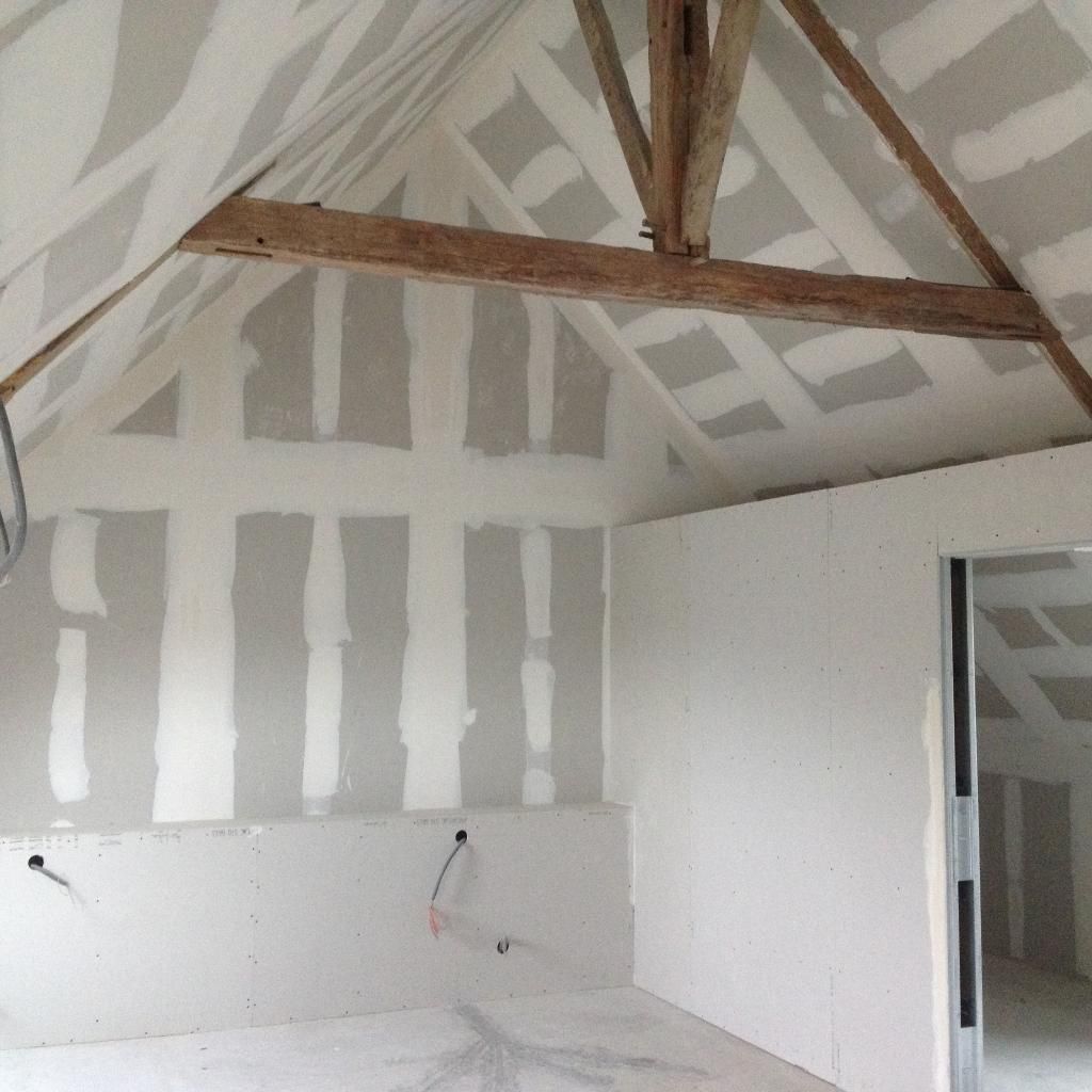 Vue intérieure d'une pièce en construction avec poutres apparentes, cloisons sèches et murs non finis.