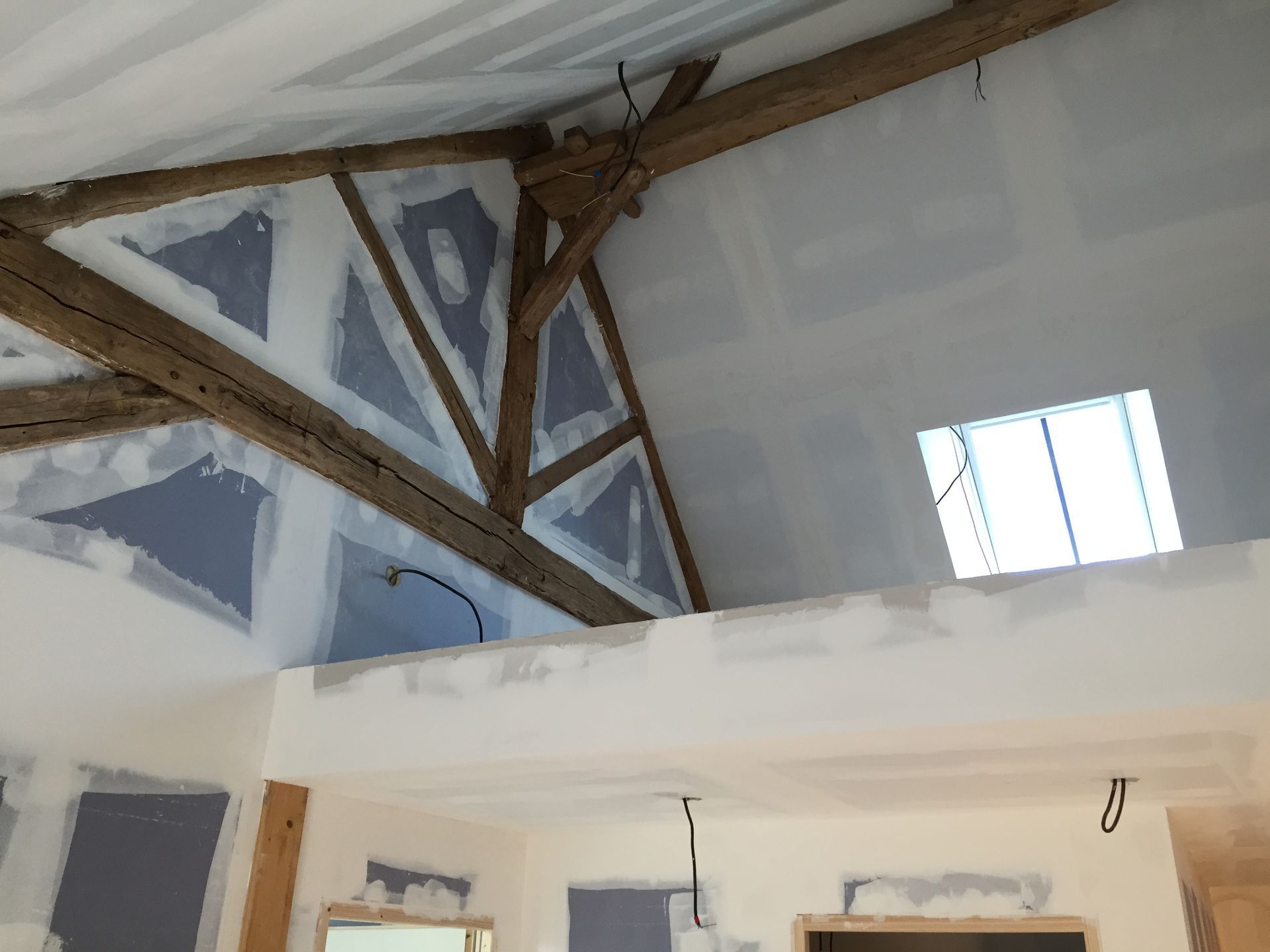 Vue intérieure d'une pièce en construction avec poutres en bois apparentes, cloisons sèches et puits de lumière.