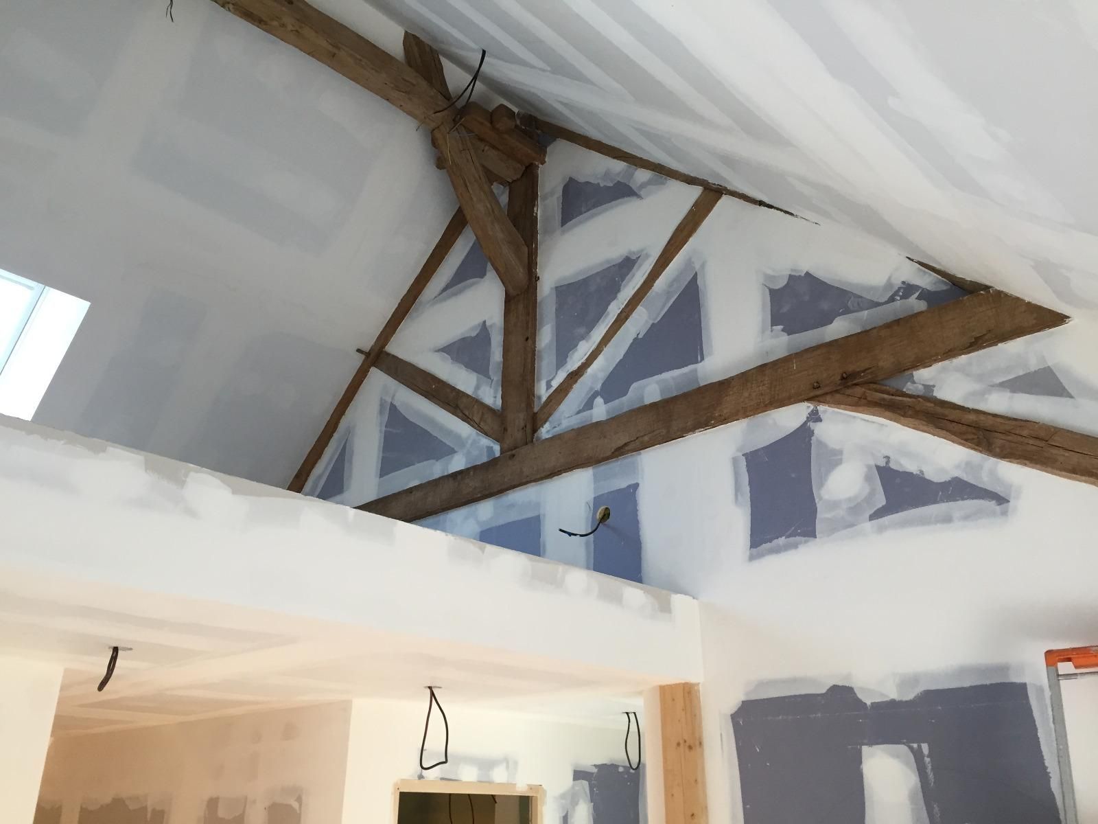 Vue intérieure d'un bâtiment en rénovation, avec poutres en bois apparentes et cloisons sèches.