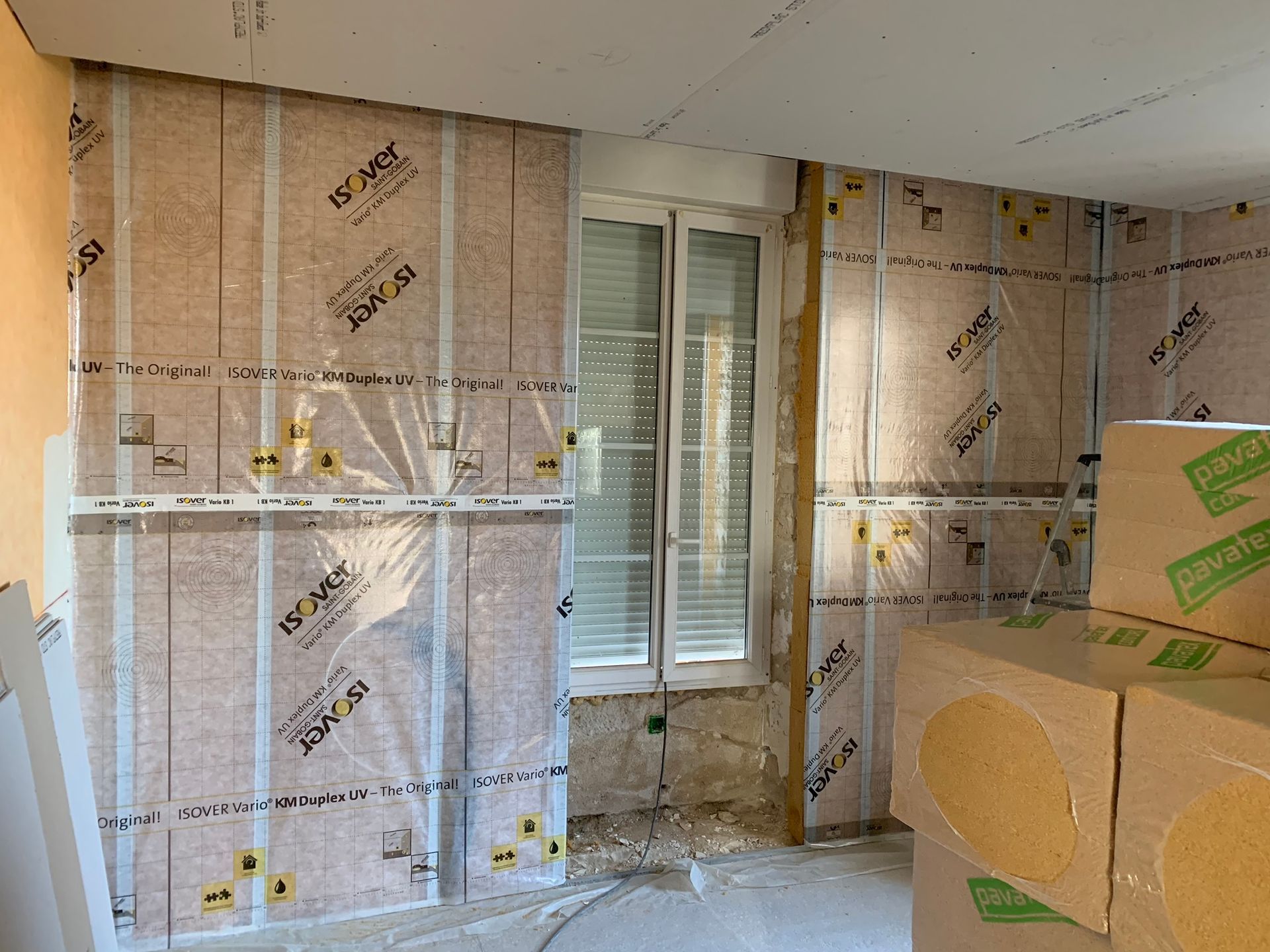 Intérieur avec murs recouverts d'isolant, fenêtre visible, travaux en cours.