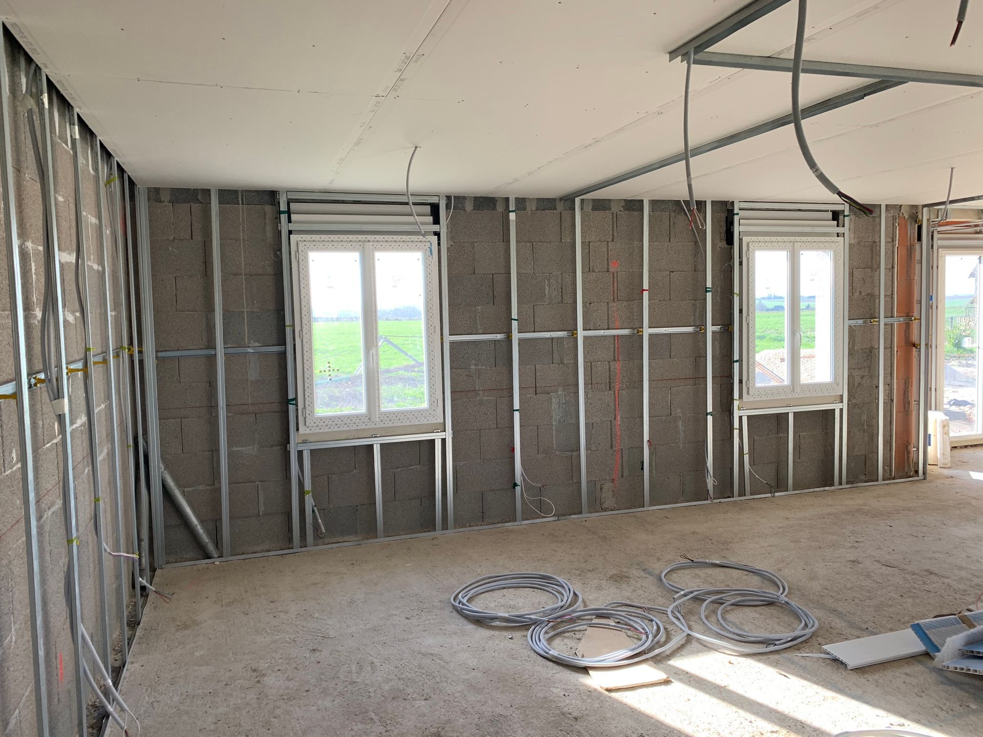 Pièce intérieure en construction, avec fenêtres et structure métallique, sol en béton.