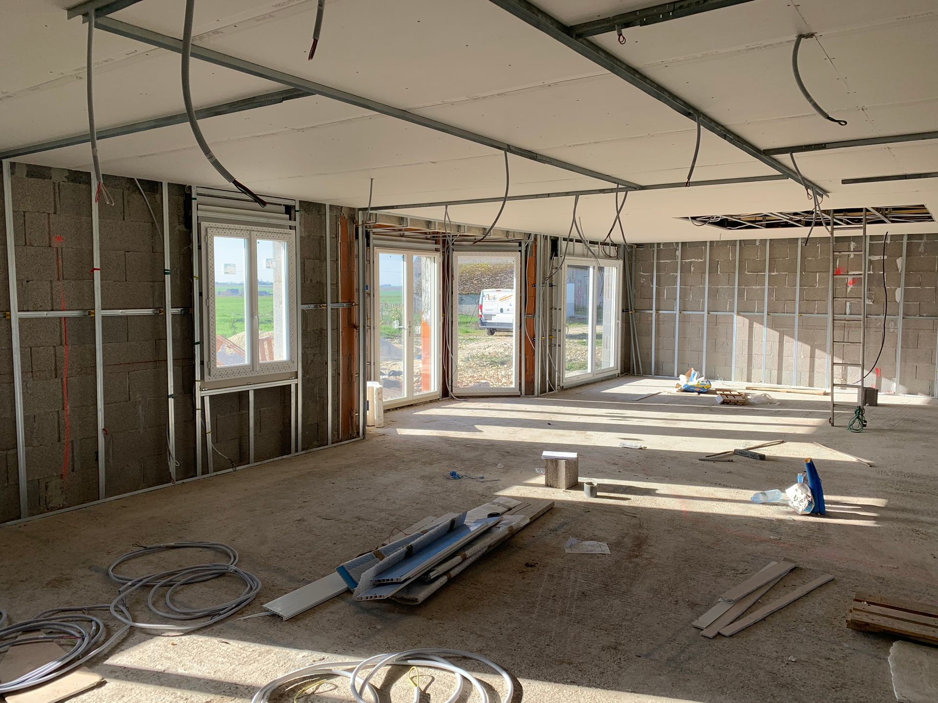 Intérieur d'une pièce en construction, avec charpente apparente, fenêtres et câblage électrique.