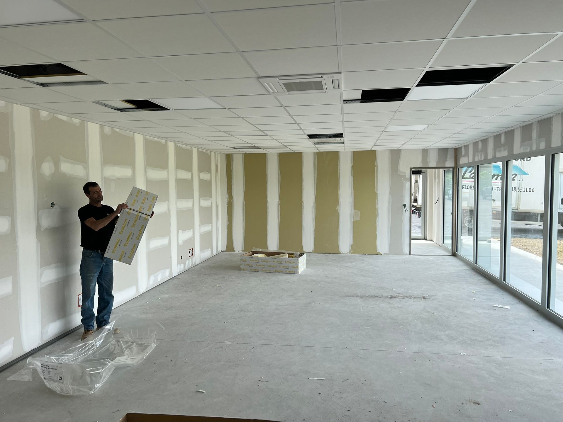 Un homme se trouve dans une pièce en construction, tenant une dalle de plafond.