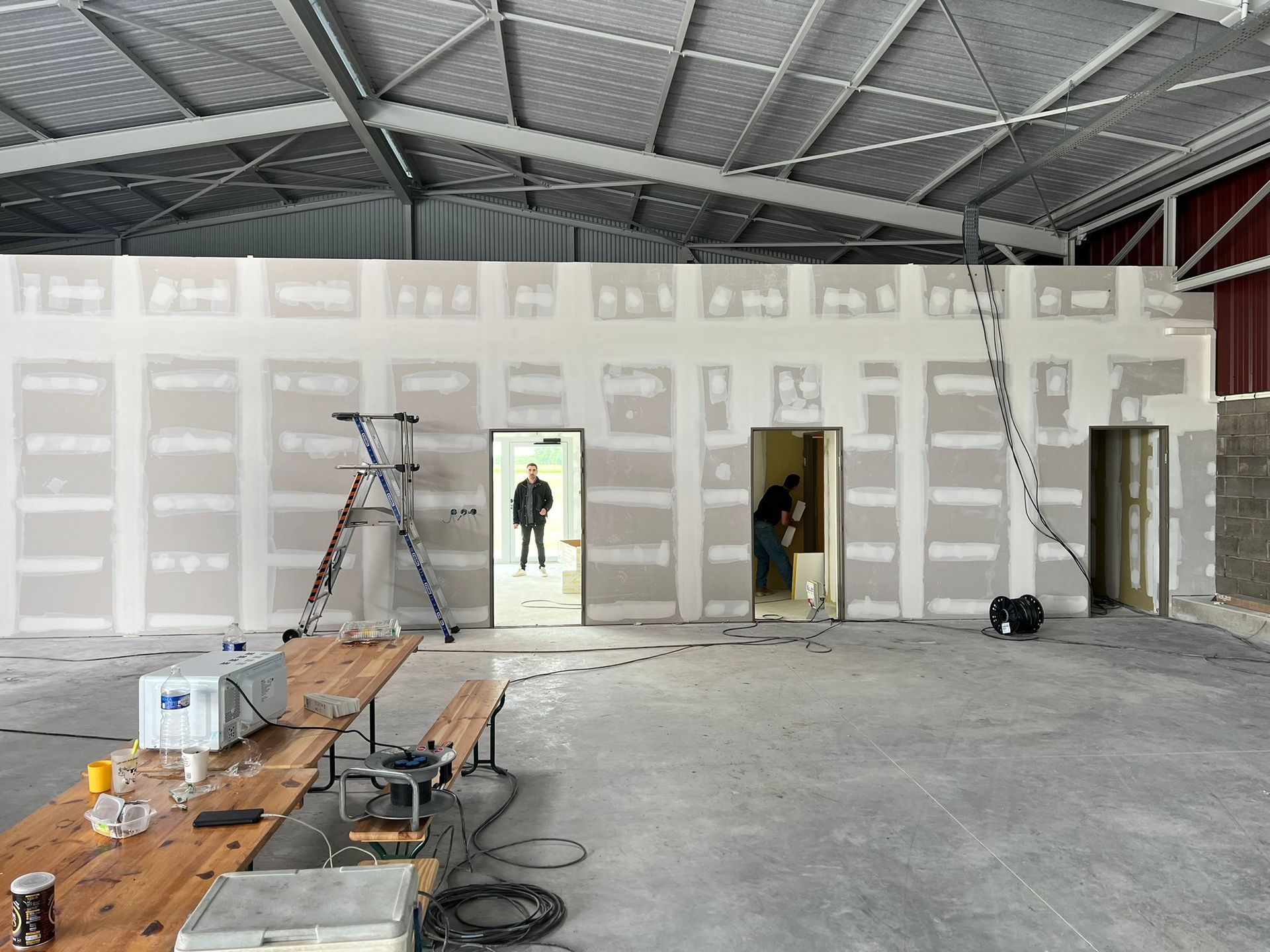 Intérieur d'un bâtiment en construction, avec des murs en plaques de plâtre et des portes ouvertes. 