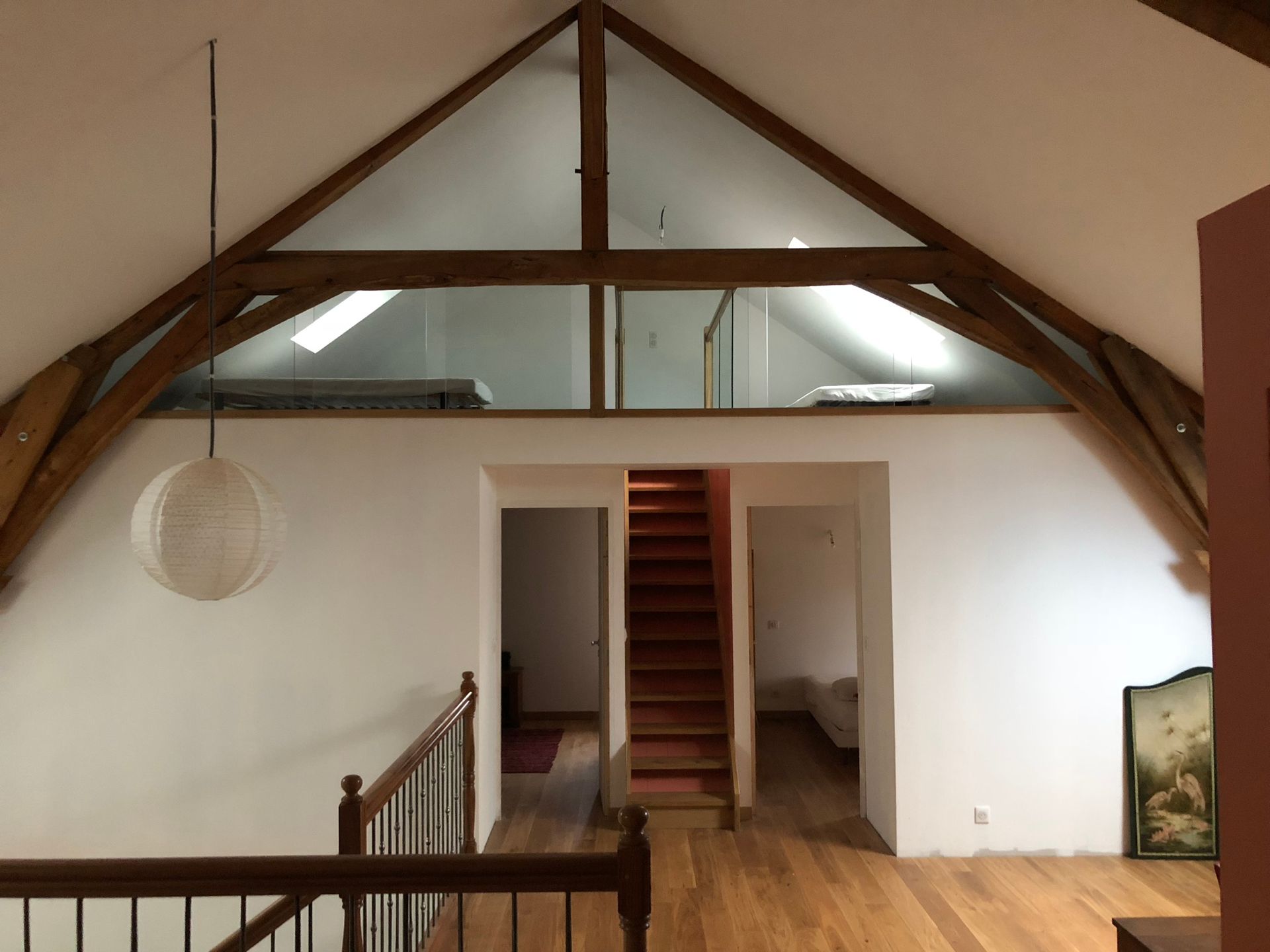 Intérieur de loft avec poutres apparentes, escalier et mezzanine. Murs blancs et luminaire sphérique.
