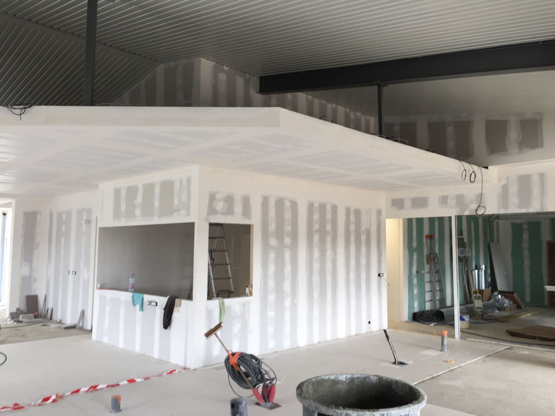 Chantier de construction intérieur avec murs et plafond en plaques de plâtre ; outils et matériaux présents.