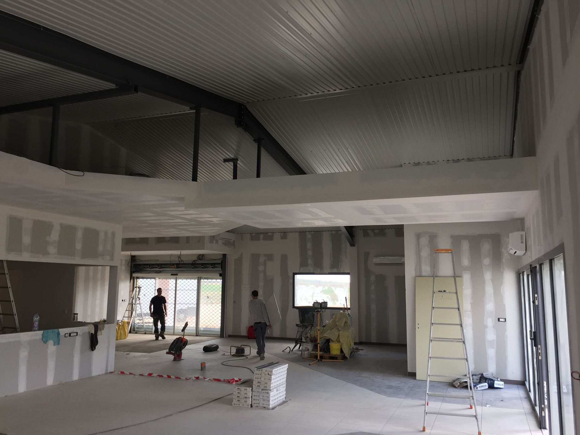 Chantier de construction intérieur avec ouvriers. Murs en plaques de plâtre, toiture métallique.