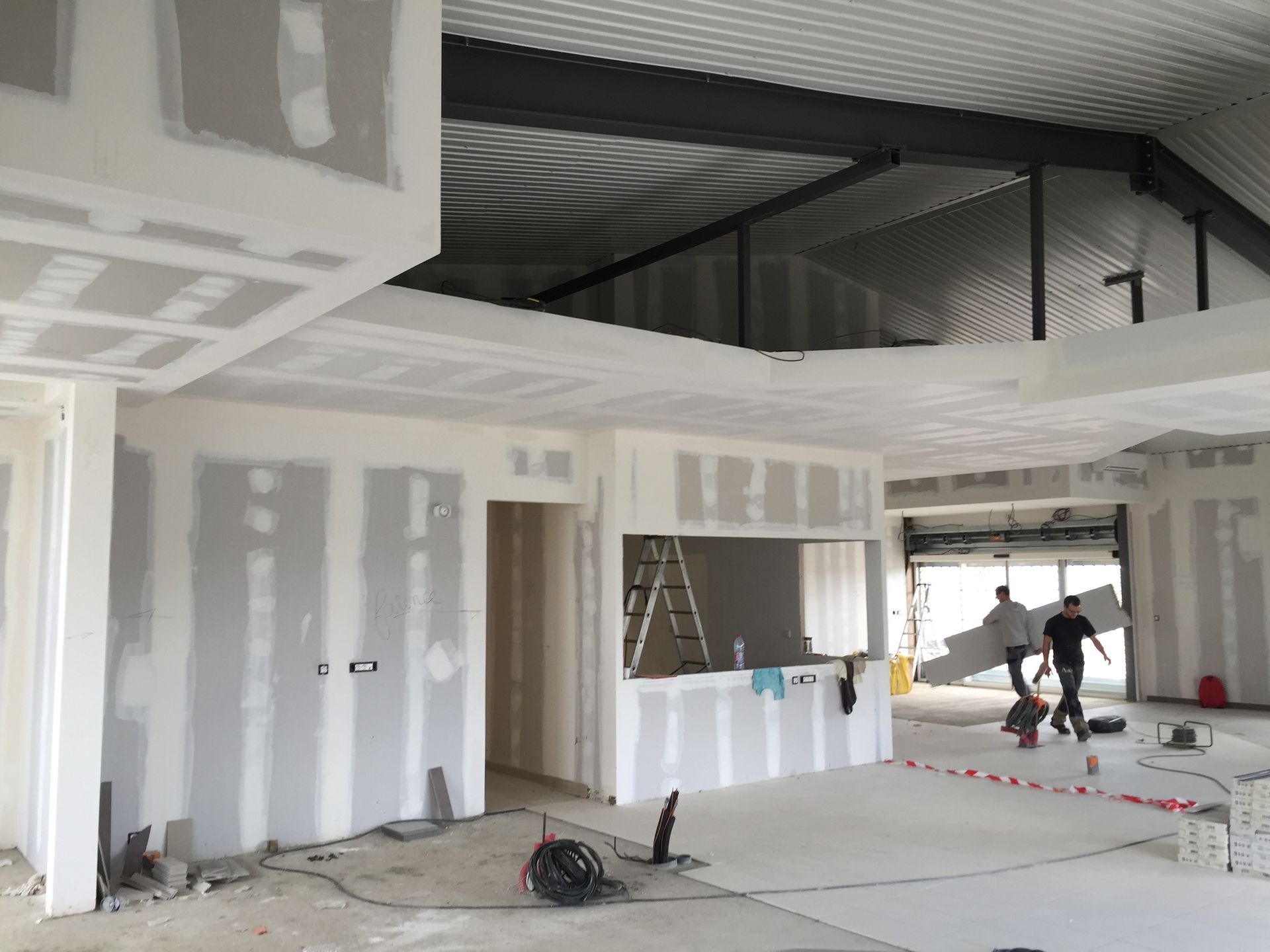 Chantier de construction intérieure avec pose de cloisons sèches. Des ouvriers transportent des planches.