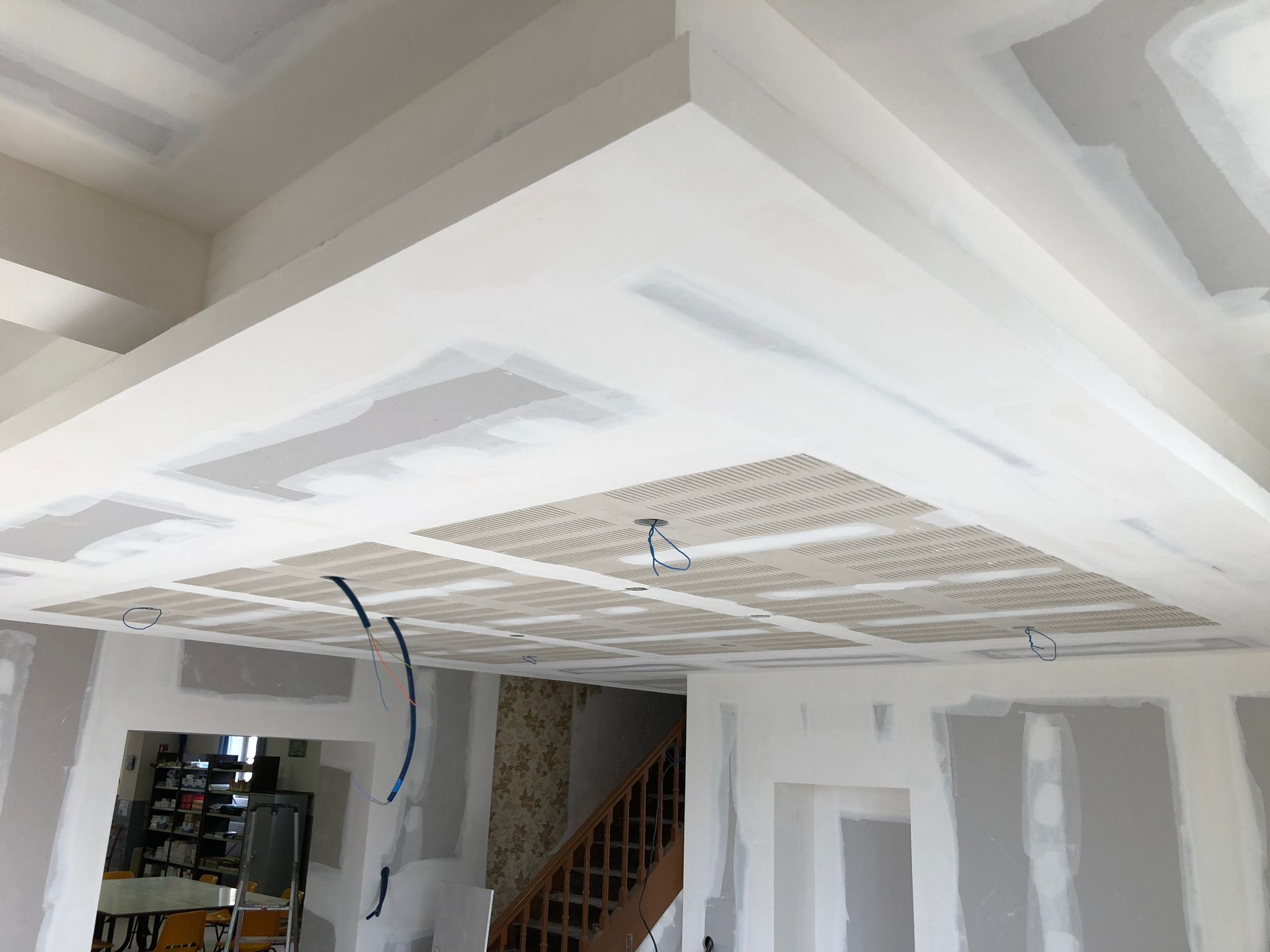 Plafond en construction avec zones d'éclairage encastrées ; cloisons sèches et câblage apparents visibles.