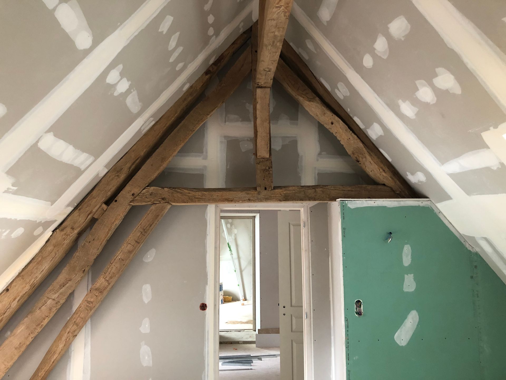 Pièce sous combles avec poutres apparentes et cloisons sèches. Une porte ouverte donne sur une autre pièce.