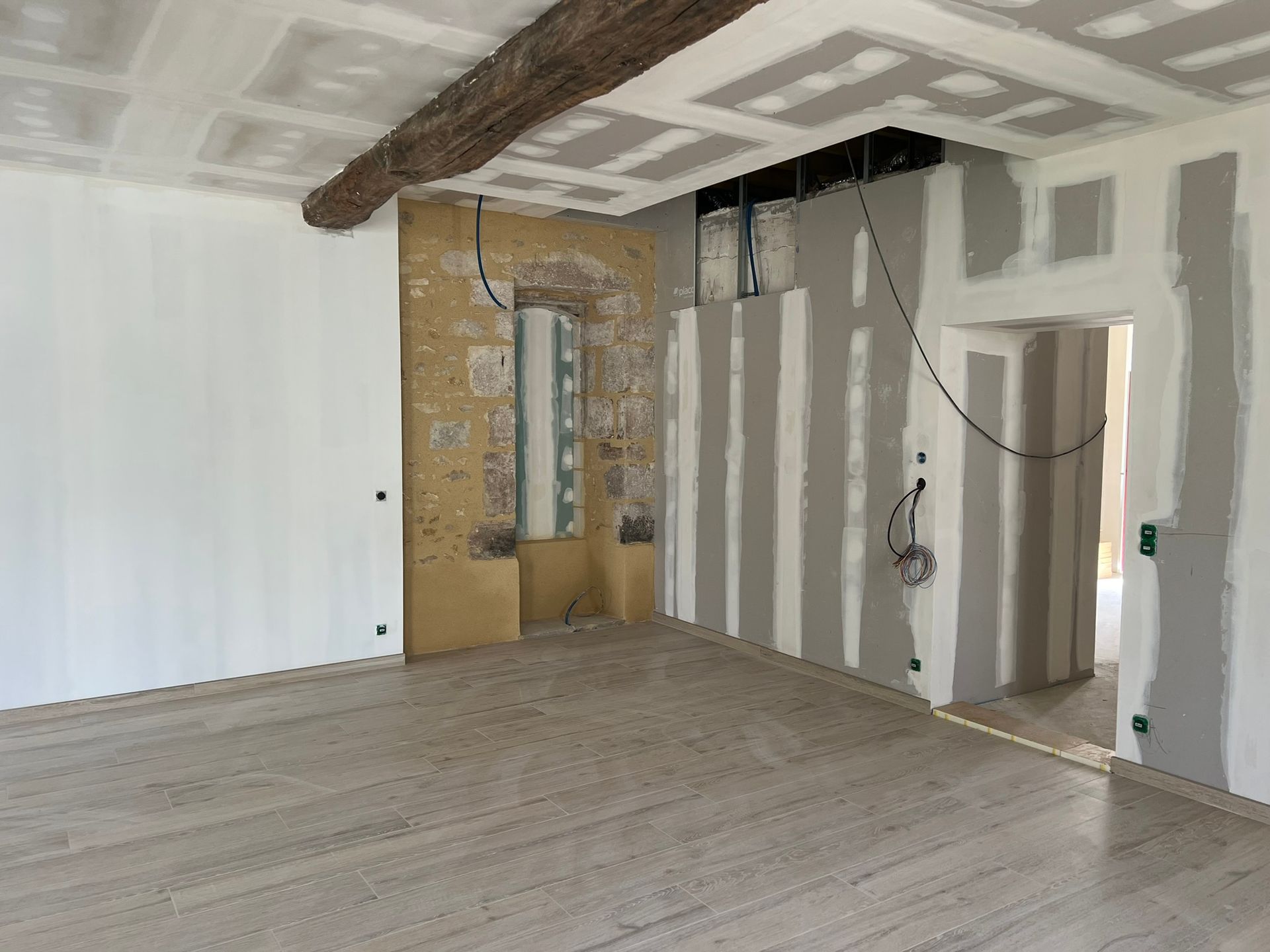 Rénovation de la pièce en cours : cloisons sèches, poutre apparente, parquet, murs partiellement finis.