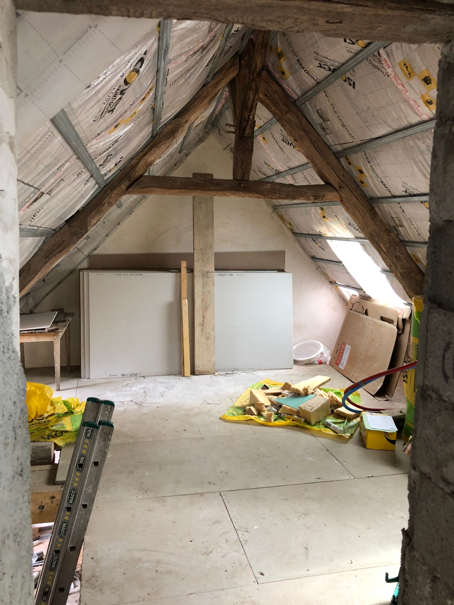 Intérieur du grenier avec poutres apparentes, isolation, cloisons sèches et matériaux de construction.