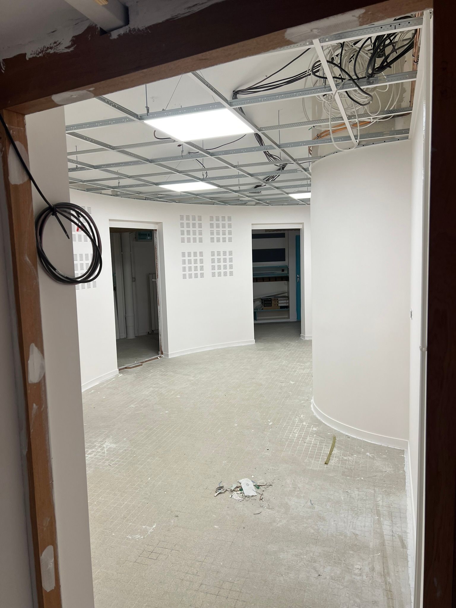 Vue intérieure d'un bâtiment en construction, montrant des pièces avec plafond apparent et sols non finis.