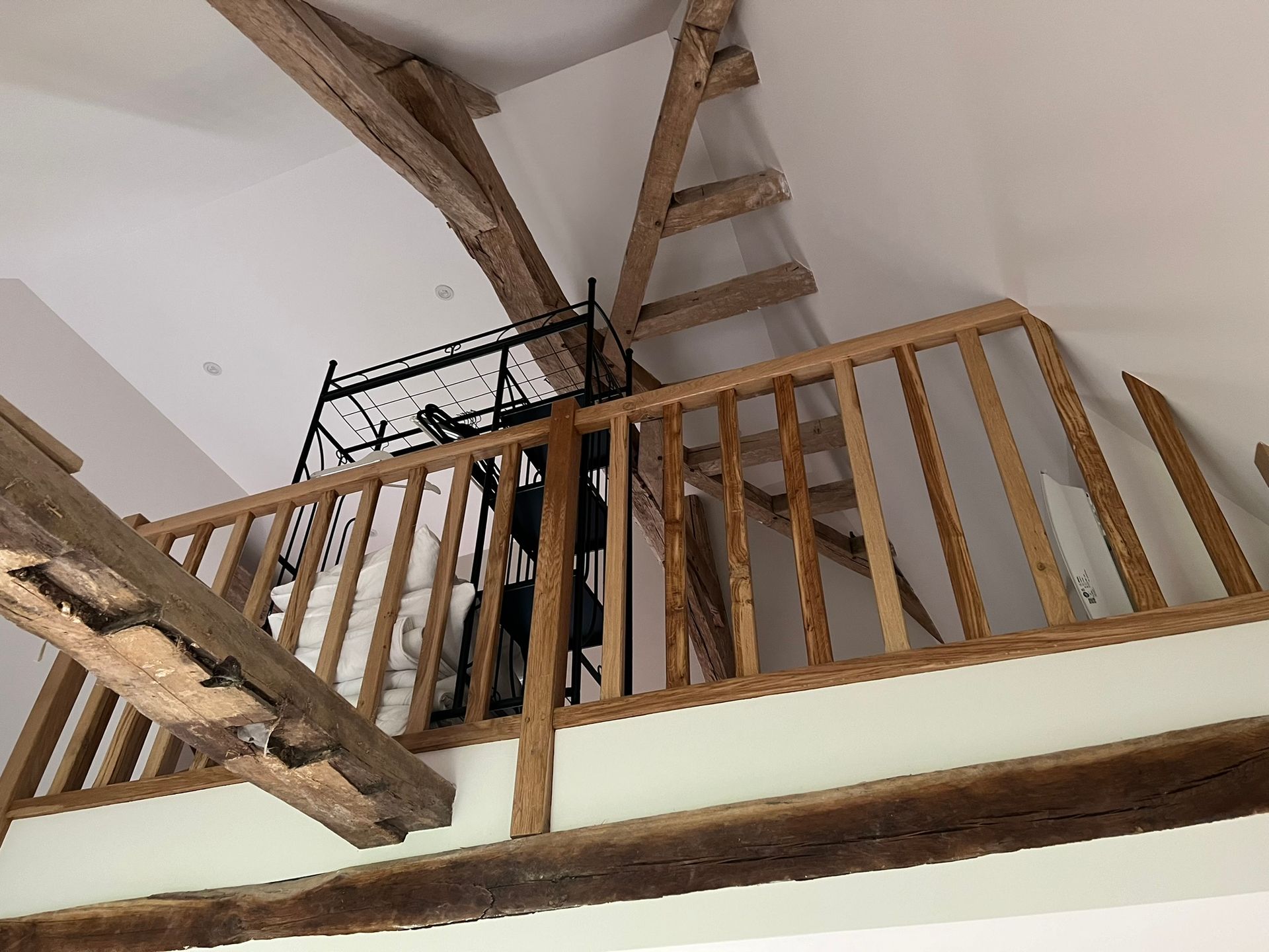 Mezzanine en bois avec rambarde, échelle et poutres apparentes, dans un intérieur aux murs blancs.