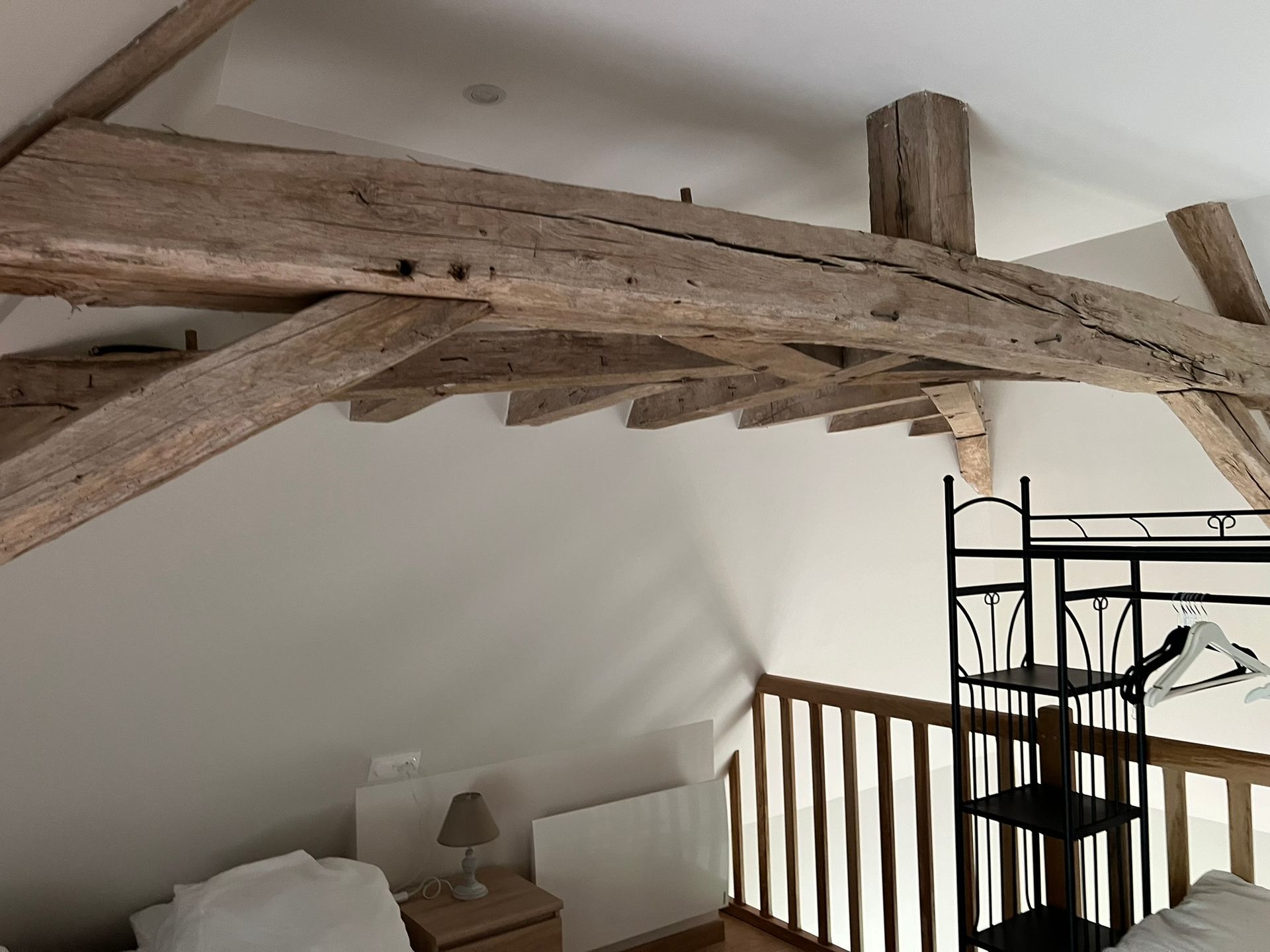 Poutres apparentes au plafond d'une chambre avec une rambarde, une étagère et un lit avec une table de chevet.