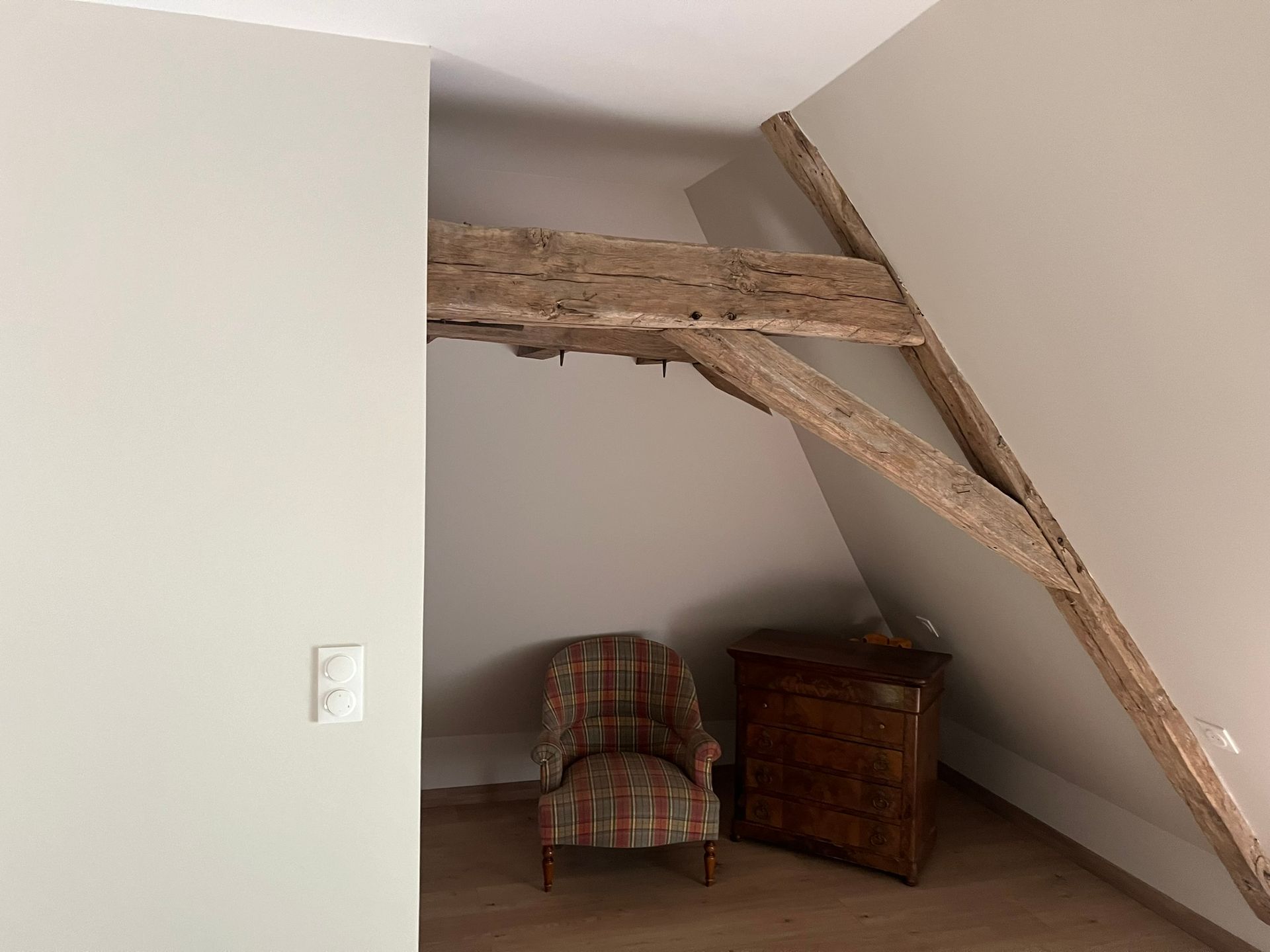 Pièce avec poutre apparente, fauteuil et armoire en bois, contre un mur incliné.