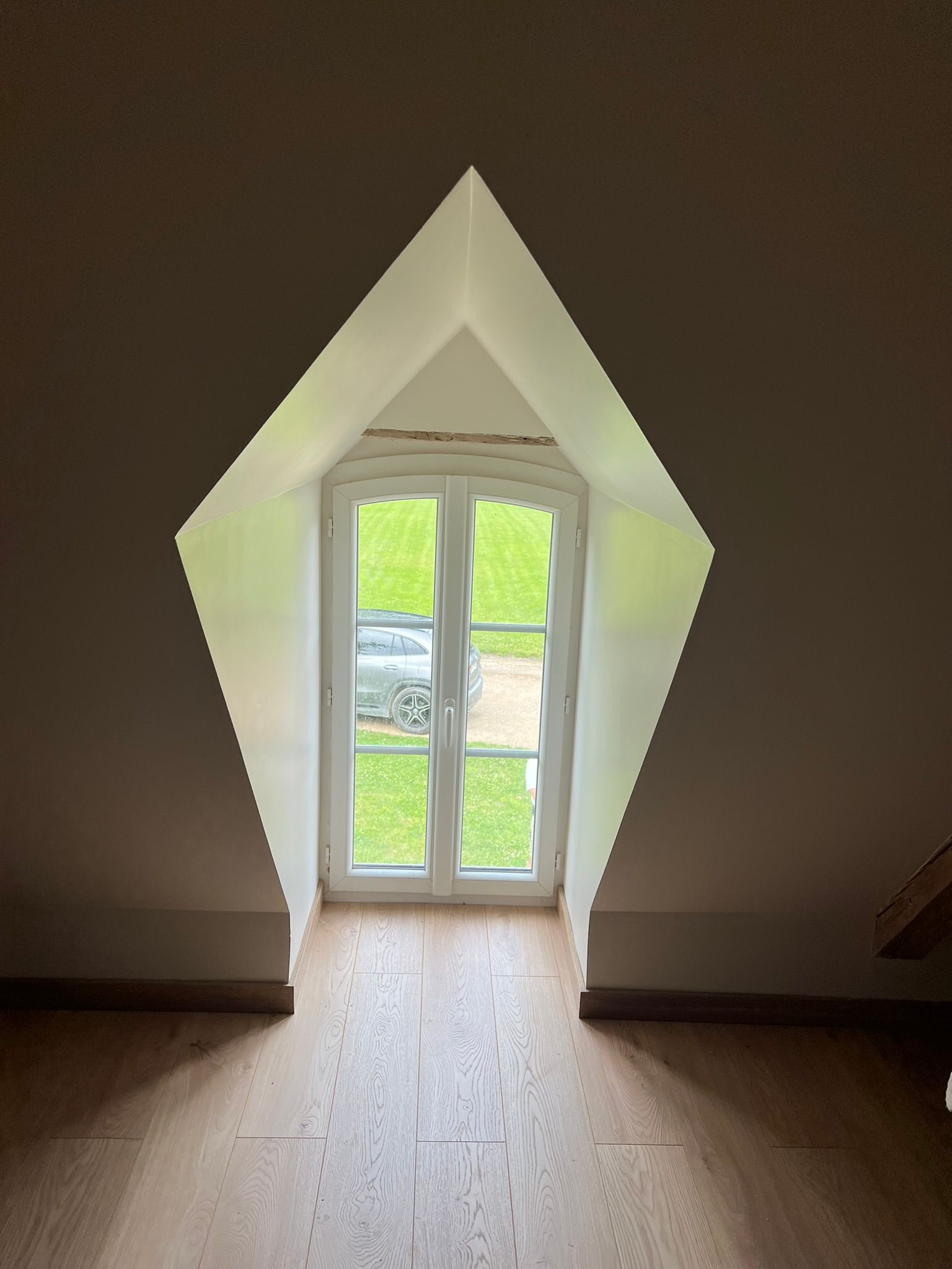 Fenêtre en forme de losange dans un grenier, offrant une vue sur la verdure.