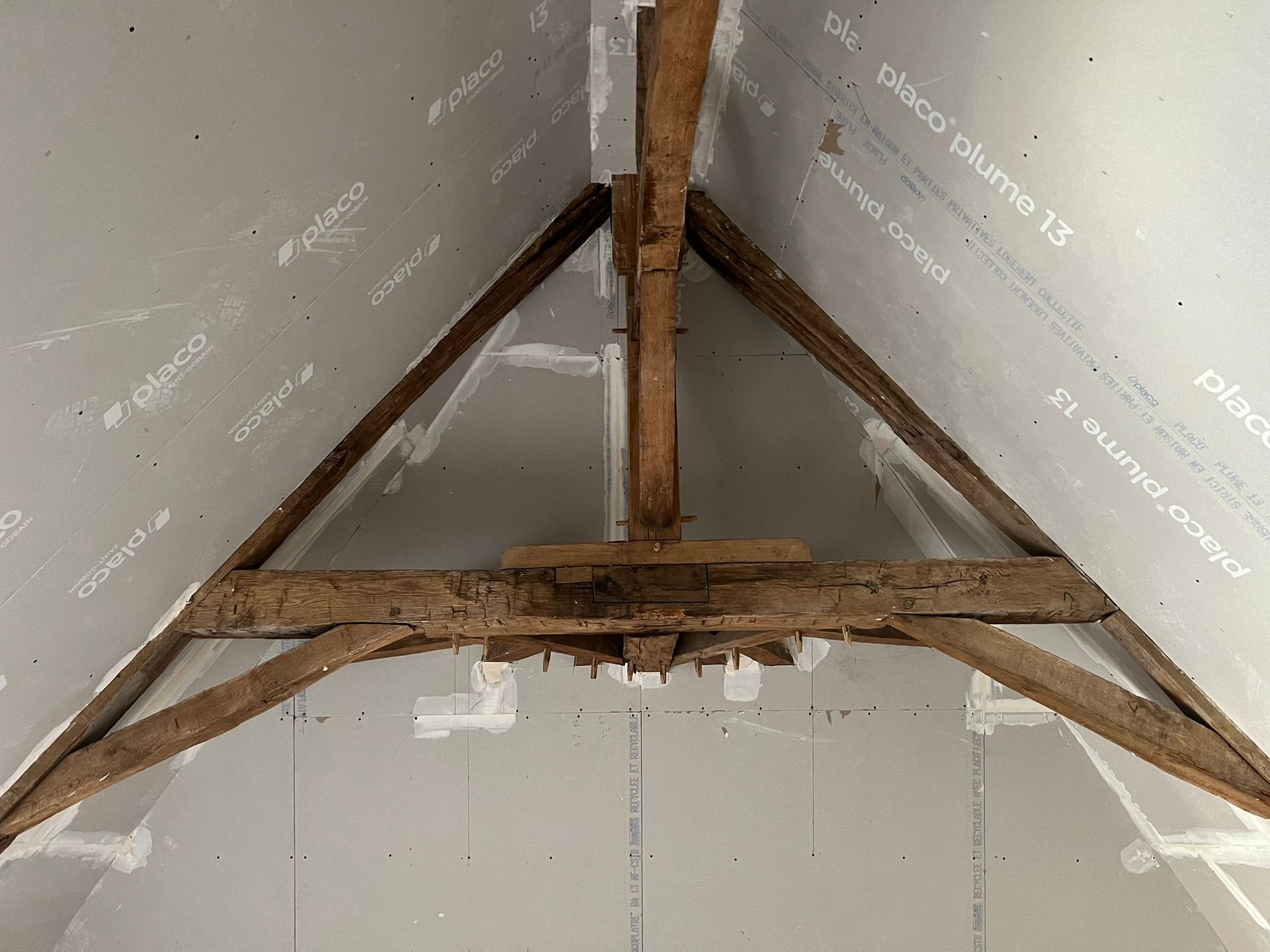Charpente en bois dans un grenier avec panneaux isolants blancs partiellement installés.