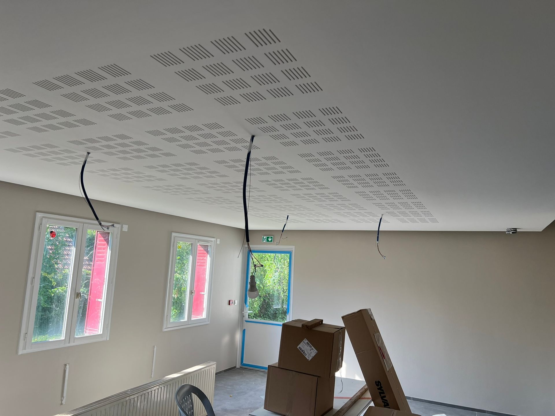 Vue intérieure d'une pièce en construction avec plafond perforé, murs inachevés et fils électriques.