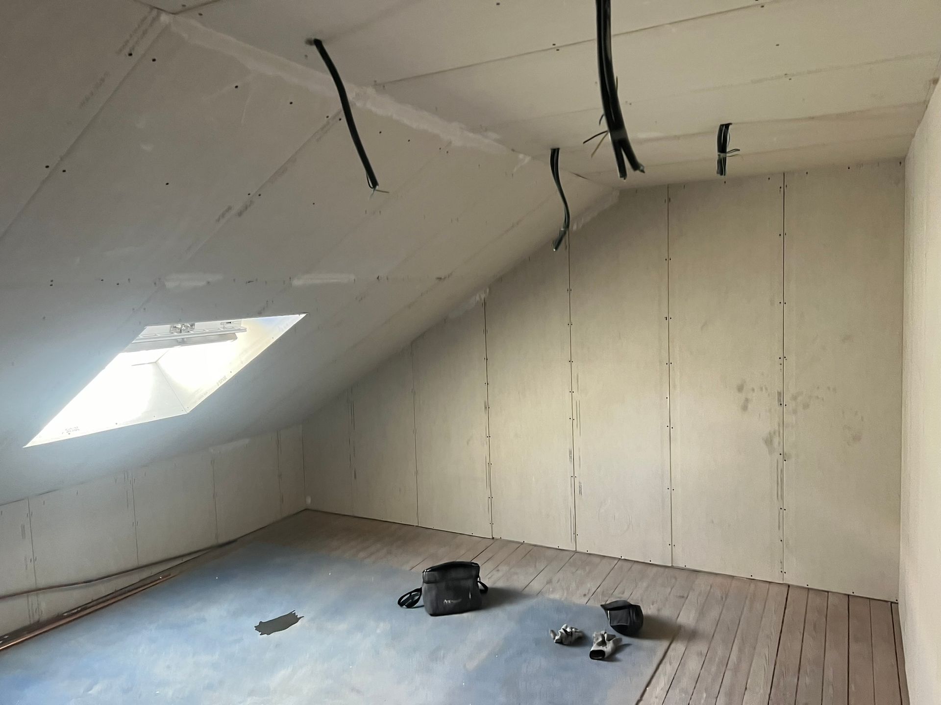 Intérieur d'un grenier non aménagé avec cloisons sèches et câblage électrique apparent.