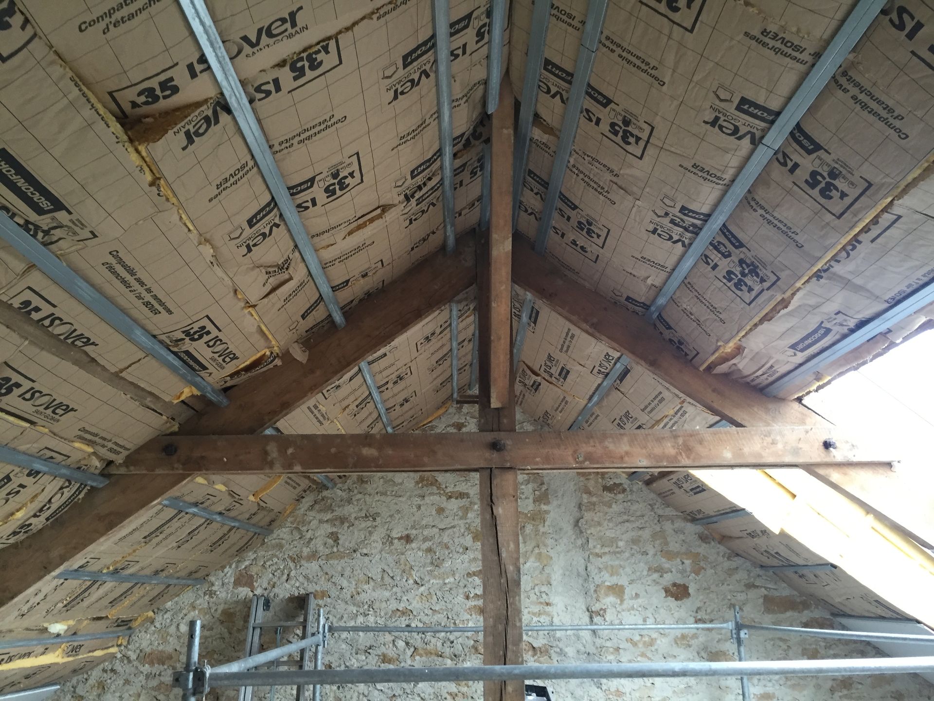 Vue intérieure d'un grenier avec poutres en bois apparentes, isolation et entretoises métalliques.