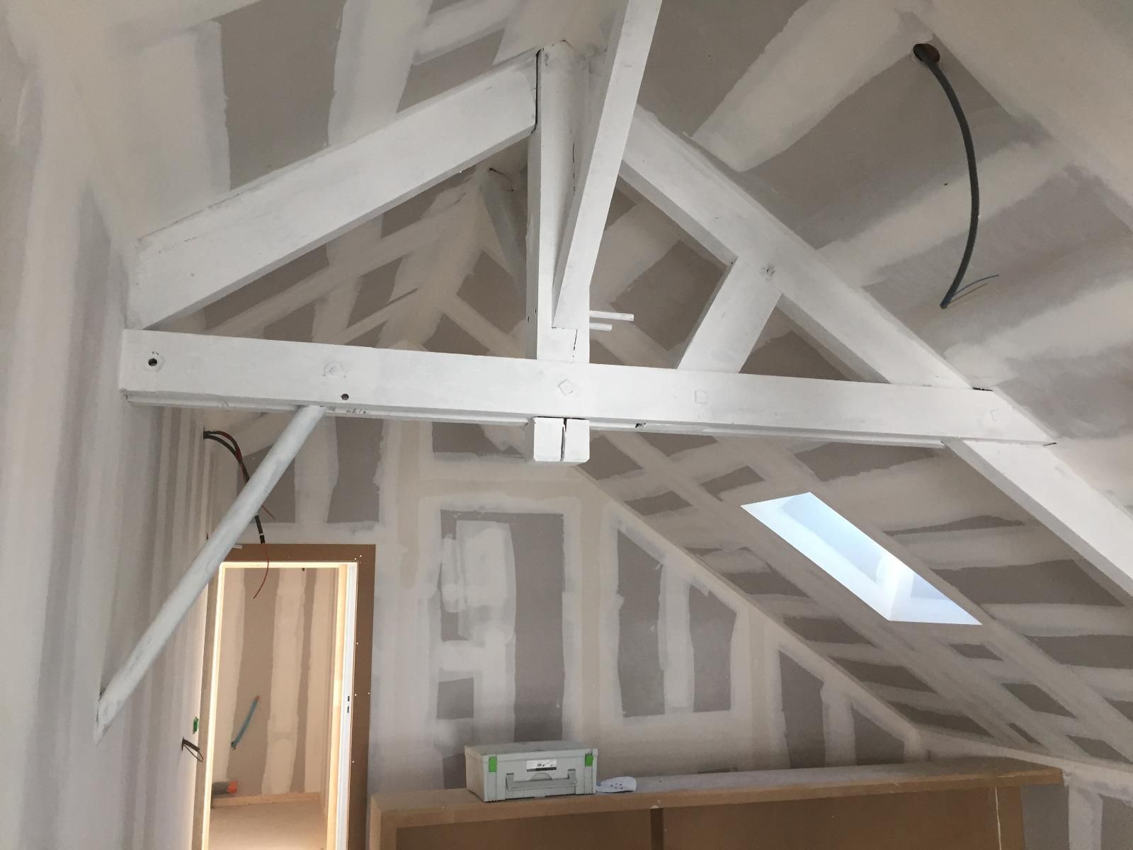 Poutres en bois peintes en blanc et cloisons sèches dans une pièce en construction.