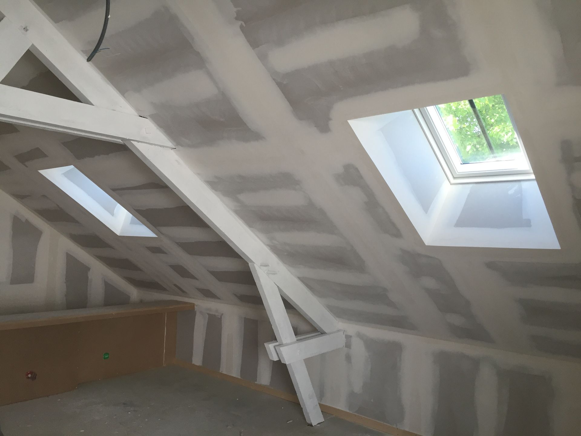 Intérieur d'un grenier avec cloisons sèches, poutres apparentes et deux puits de lumière.