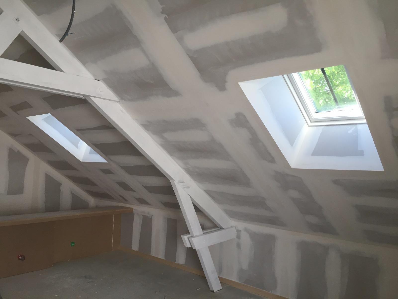 Aménagement intérieur des combles en cours, avec poutres apparentes et cloisons sèches. Deux puits de lumière.