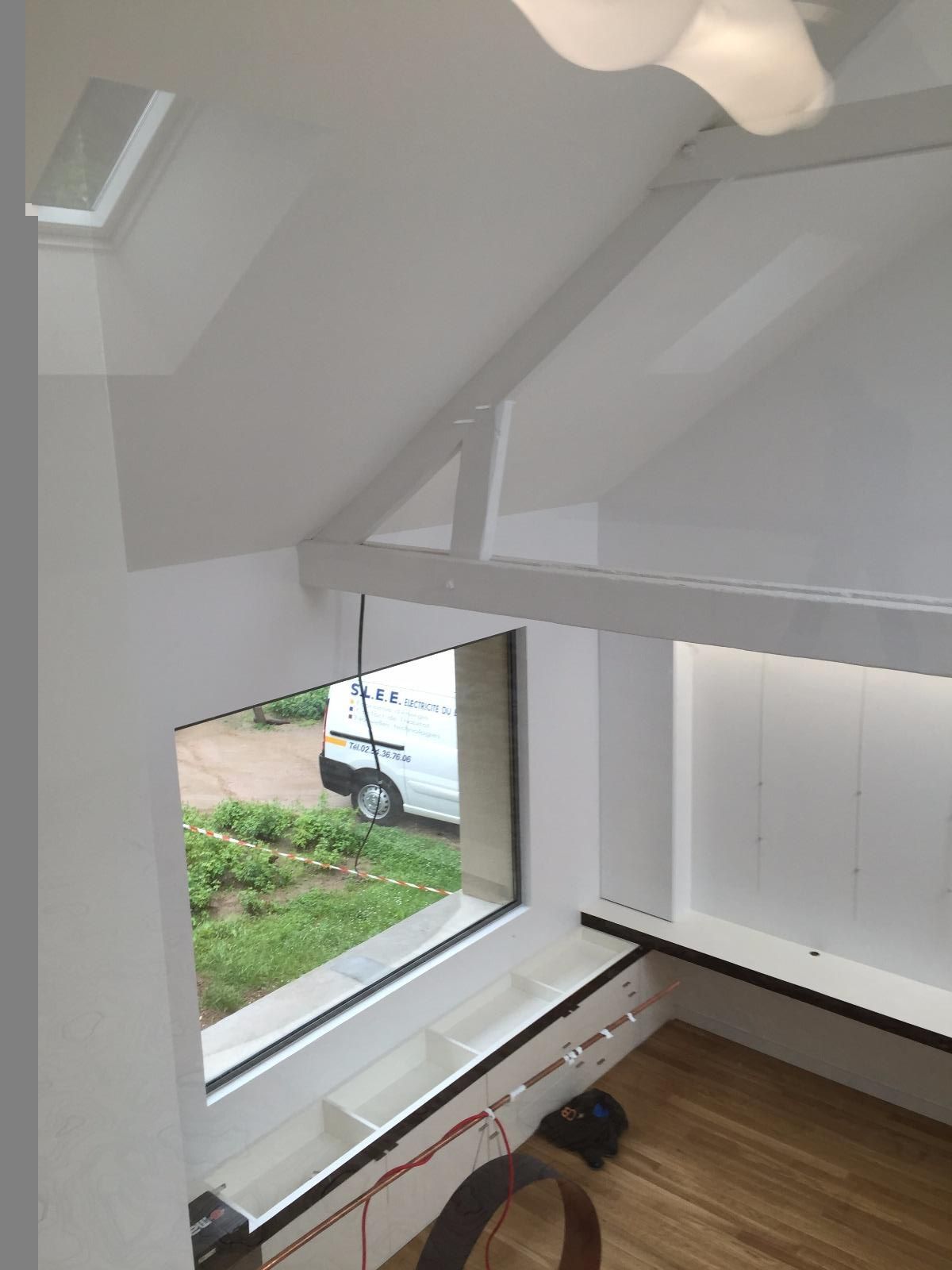 Pièce aux murs blancs avec une fenêtre. Sol et poutres apparentes au plafond.