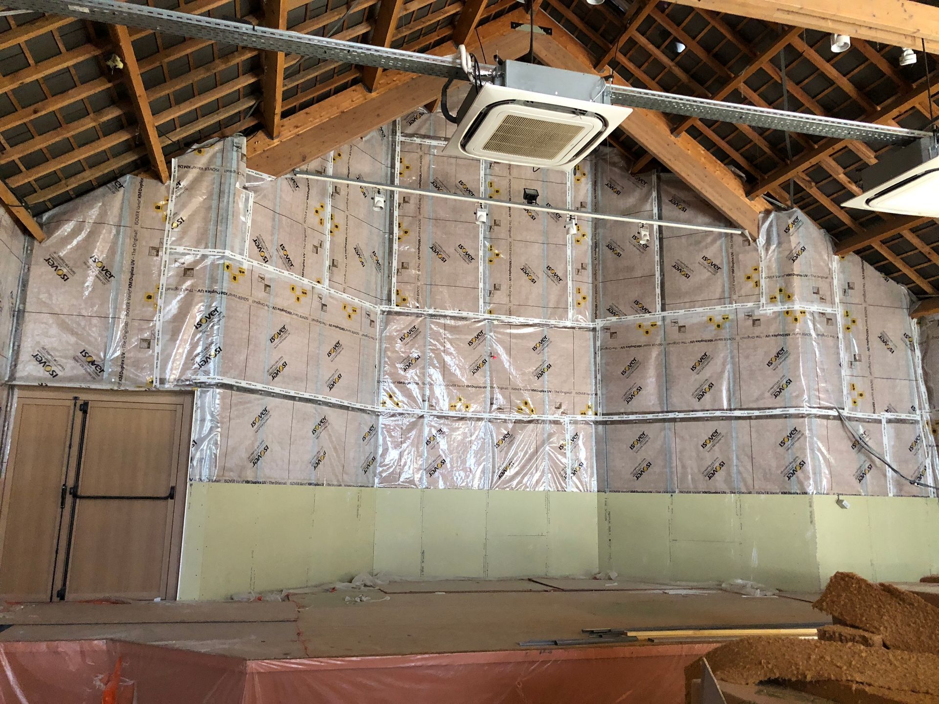 Isolation des murs intérieurs d'un bâtiment en construction, montrant la charpente, le pare-vapeur et la porte existante.