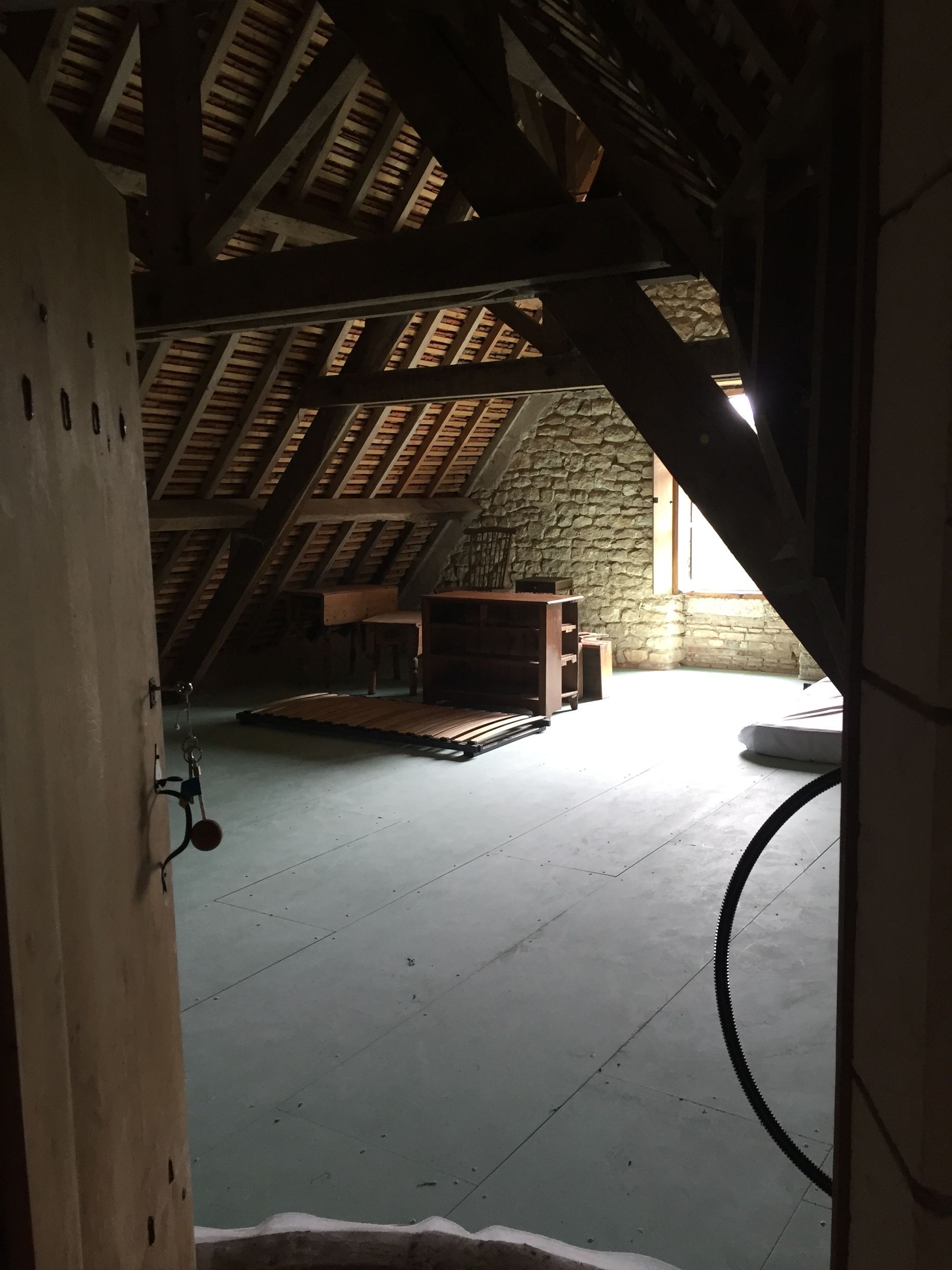 Intérieur mansardé avec poutres apparentes et mur en pierre. 