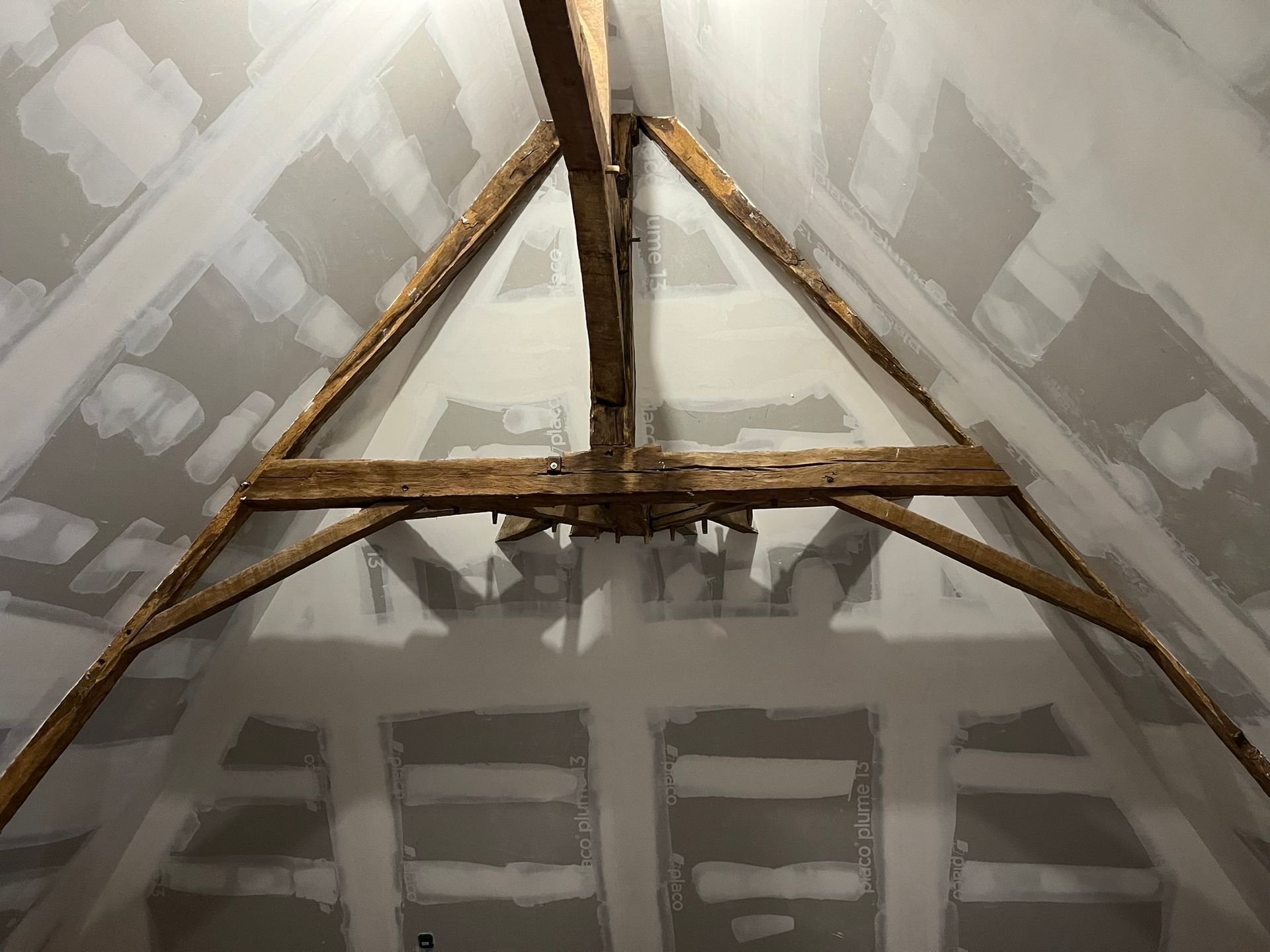 Vue intérieure d'un grenier avec des poutres apparentes en bois formant un triangle.