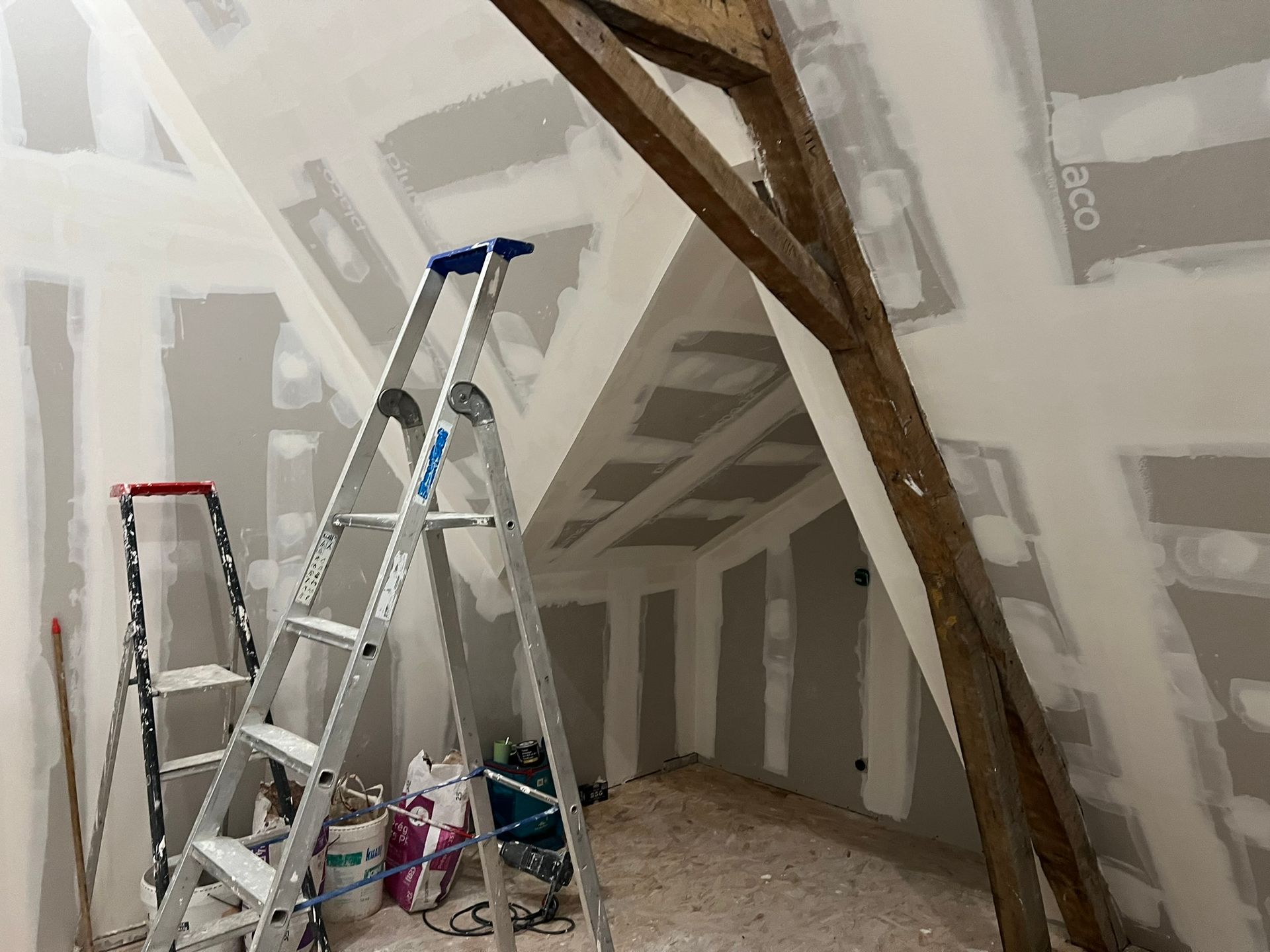 Chantier : grenier intérieur avec cloisons sèches installées, échelles, poutres en bois.