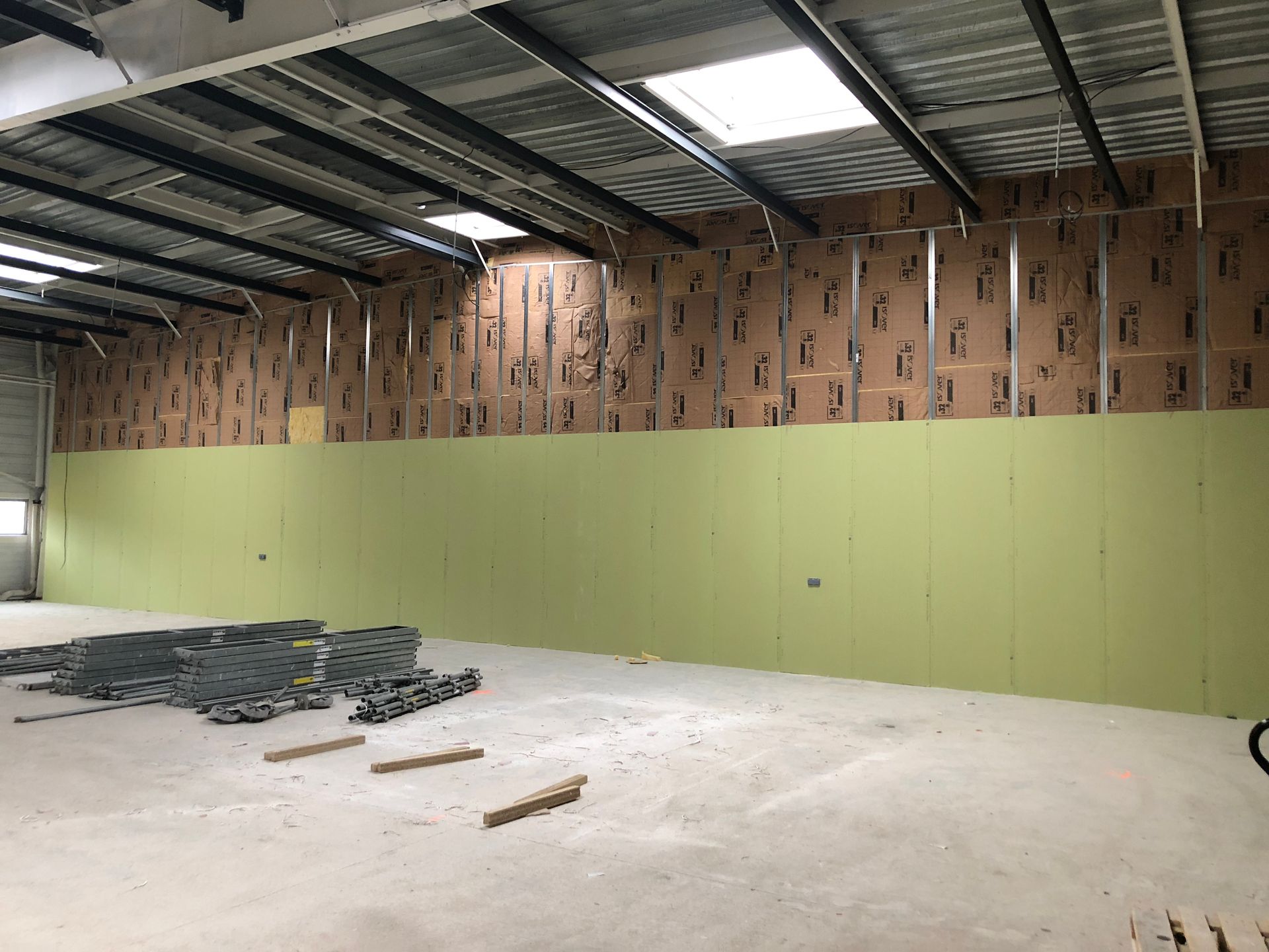 Vue intérieure d'un entrepôt en construction, montrant des murs partiellement finis avec isolation et panneaux verts.