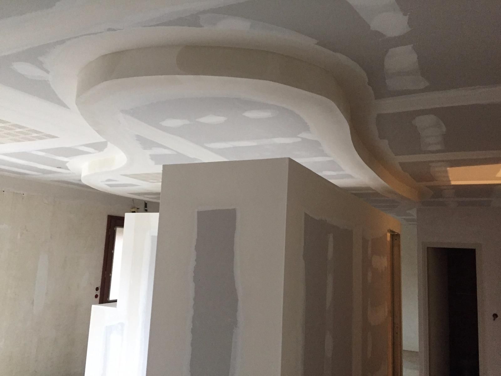 Aménagement intérieur avec plafond en plaques de plâtre incurvées. Pièce inachevée avec murs blancs, fenêtre et porte.