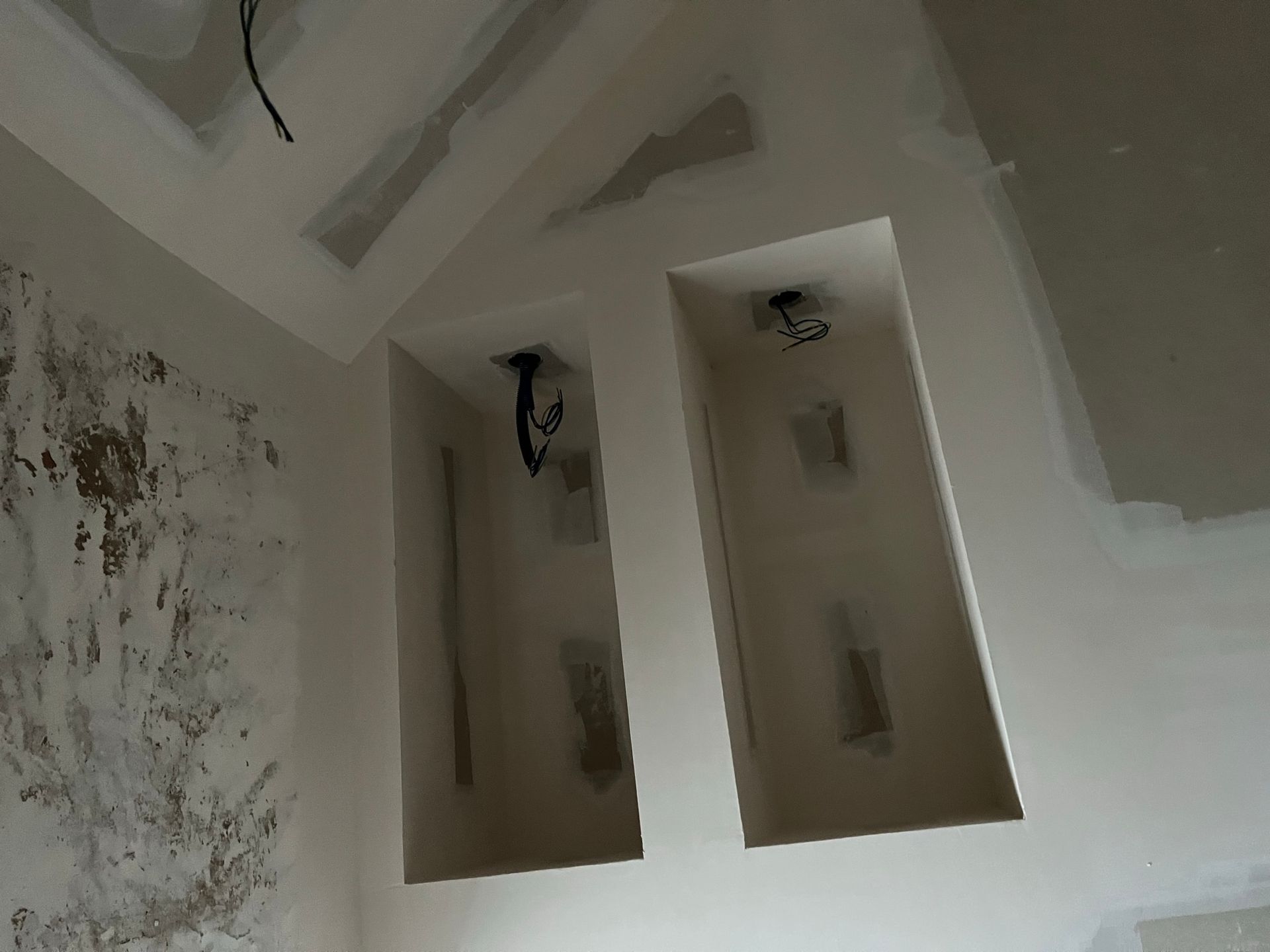 Deux niches murales encastrées avec câblage aérien, dans une pièce en construction, avec un mur partiellement plâtré.