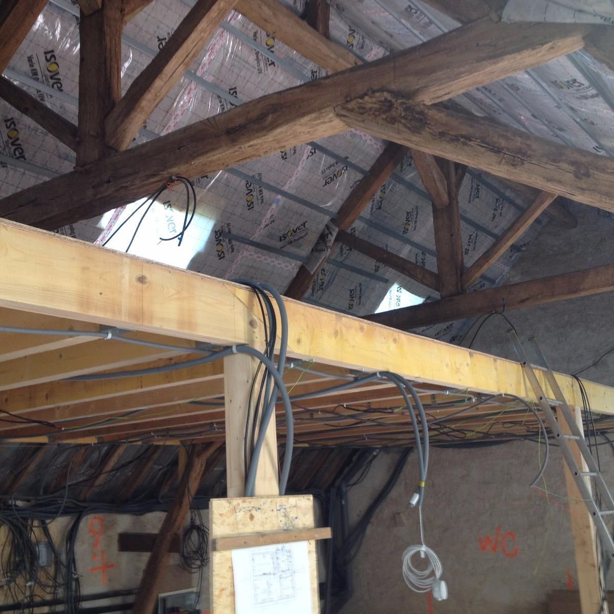 Vue intérieure d'un grenier avec poutres en bois apparentes, isolation et câblage électrique.