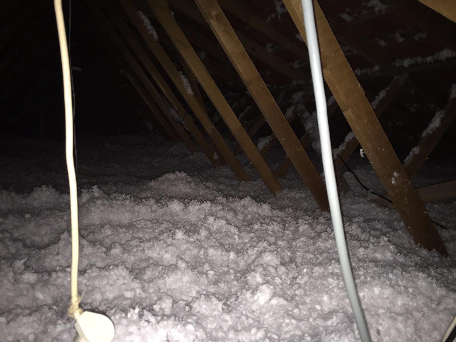 Intérieur du grenier avec poutres en bois et isolation blanche. Des fils électriques pendent.