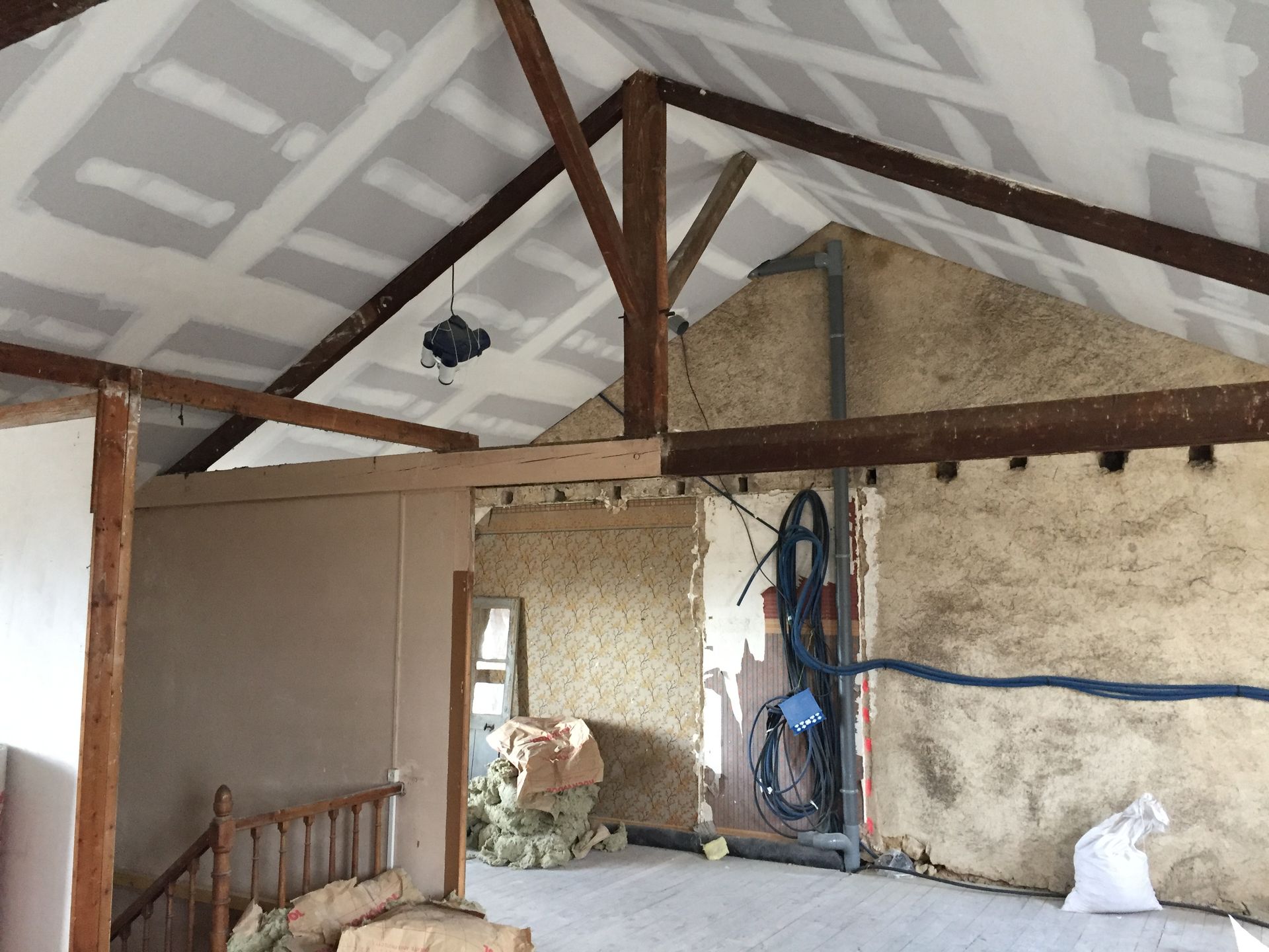 Intérieur en cours de rénovation montrant des poutres apparentes, des cloisons sèches et des murs partiellement finis.
