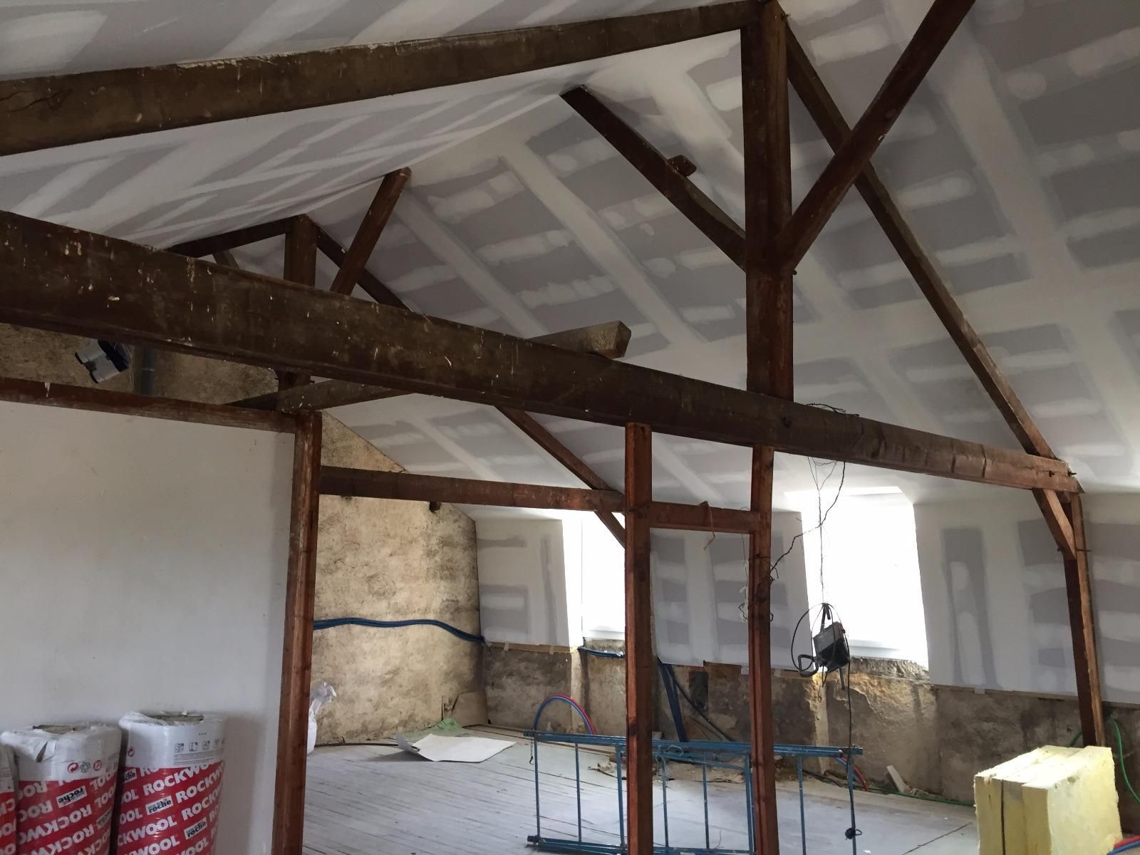 Vue intérieure d'un bâtiment en construction, montrant des poutres en bois apparentes et des cloisons sèches.