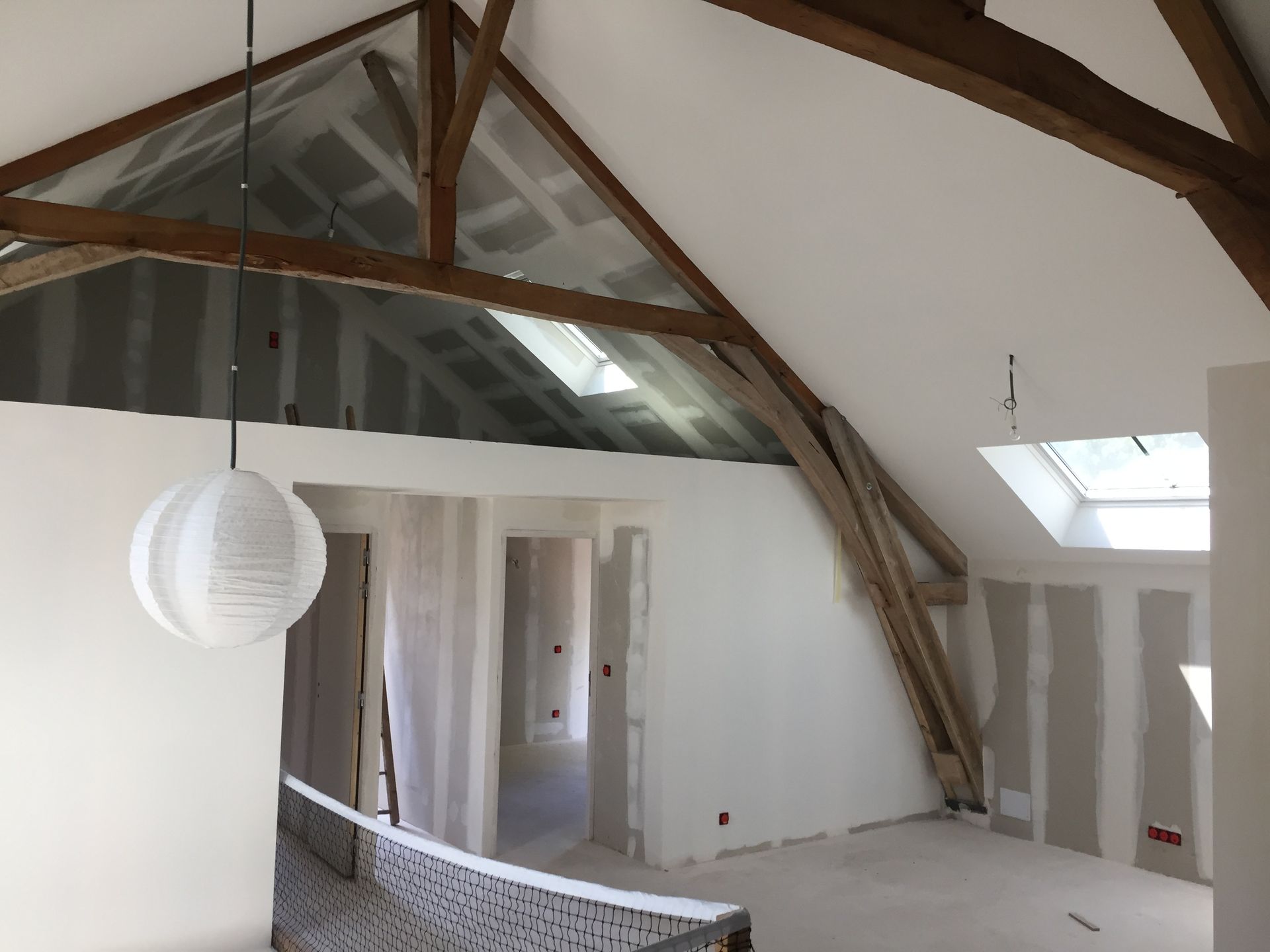 Rénovation des combles avec poutres apparentes, cloisons sèches, puits de lumière et lanterne en papier.