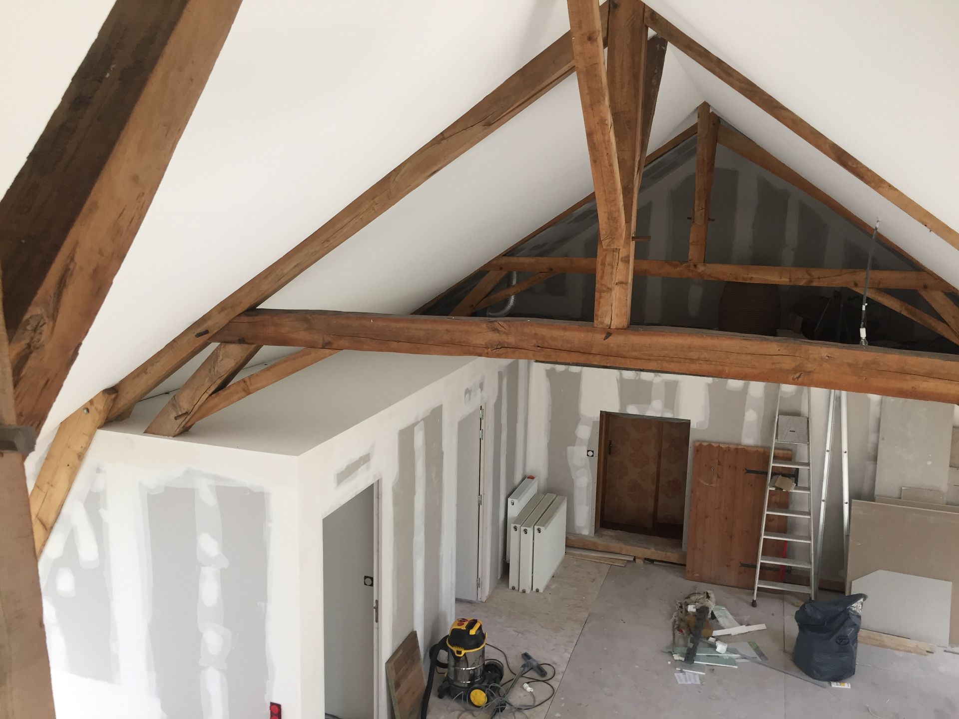 Rénovation intérieure avec poutres apparentes, cloisons sèches et une échelle.