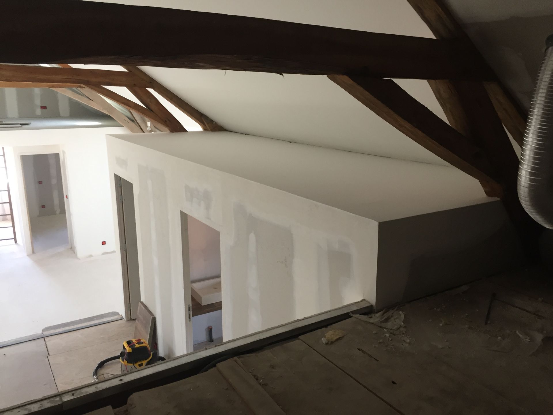 Chantier de construction avec poutres en bois apparentes, structure en plaques de plâtre et portes ouvertes.