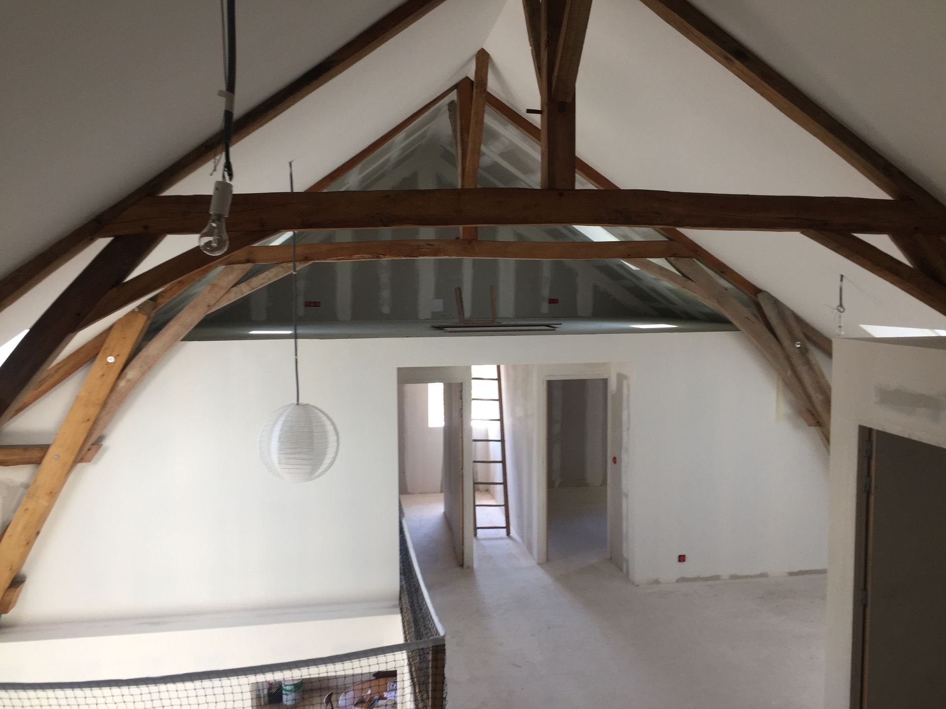 Vue intérieure d'un grenier en rénovation, montrant des poutres en bois apparentes, des murs blancs et des portes.